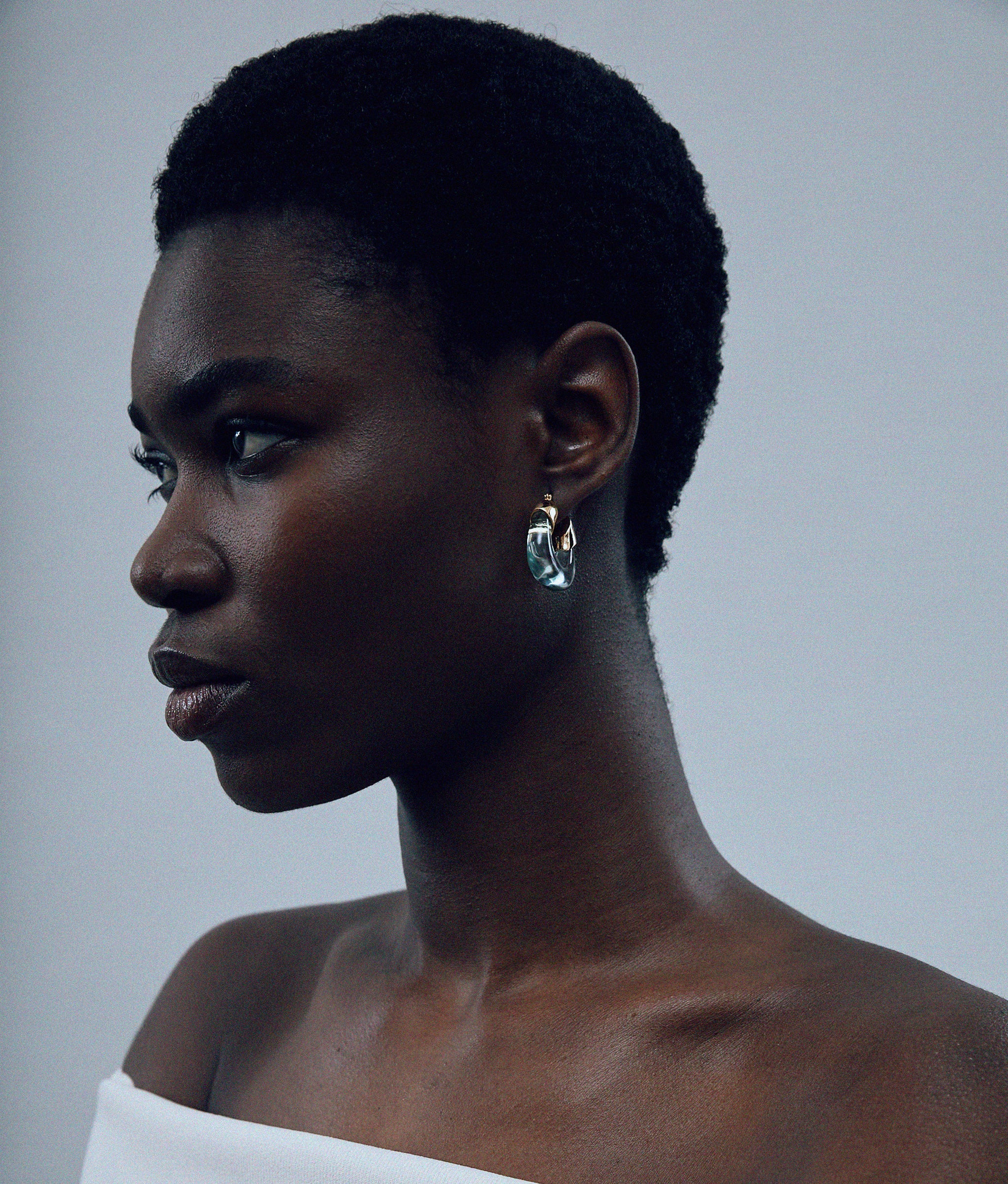 Model on grey background wearing Mini Organic Hoops in Aqua .