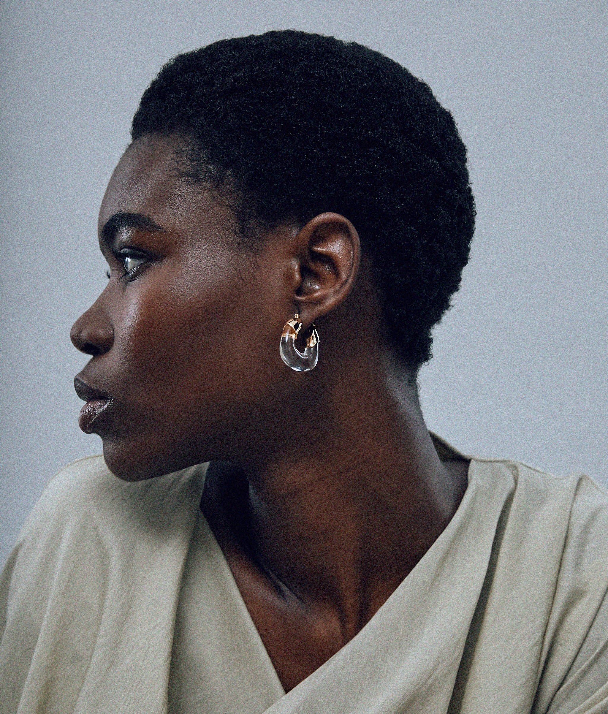 Model on grey background wearing Mini Organic Hoops in Clear.