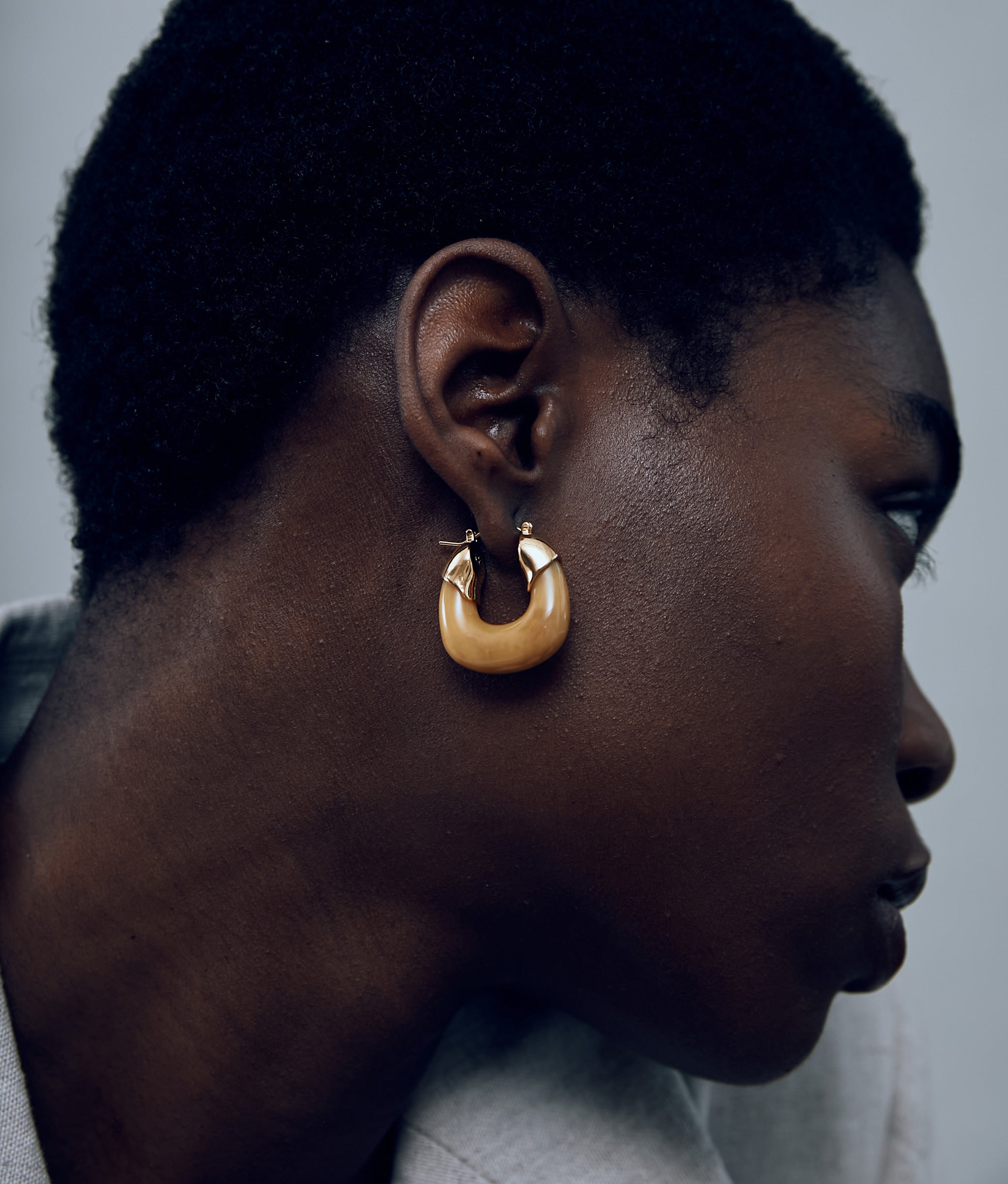 Close-up of model on grey background with the Mini Organic Hoops in Mocha.