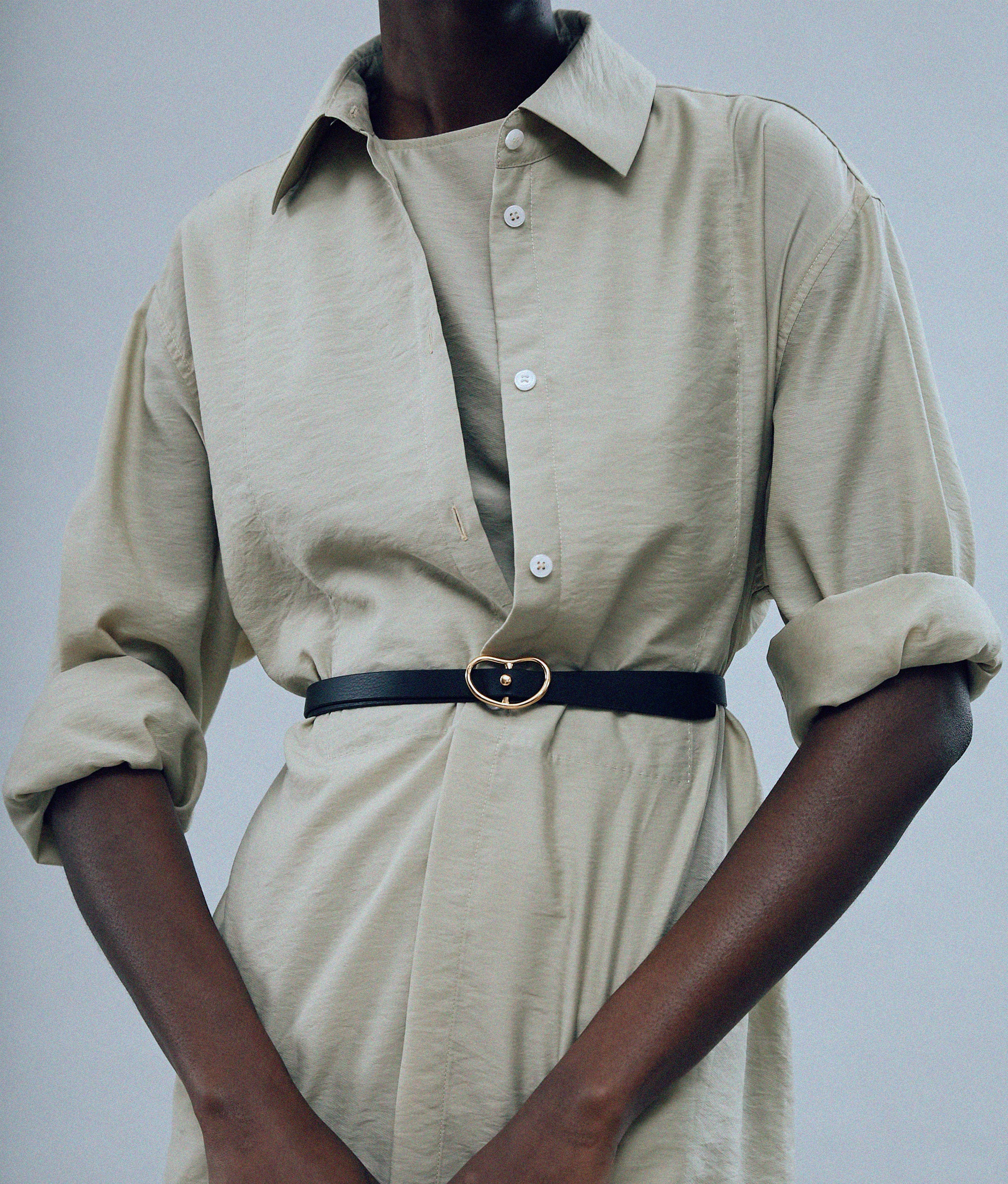 Model on grey backdrop wears tan button-down with Skinny Georgia Belt in Black.