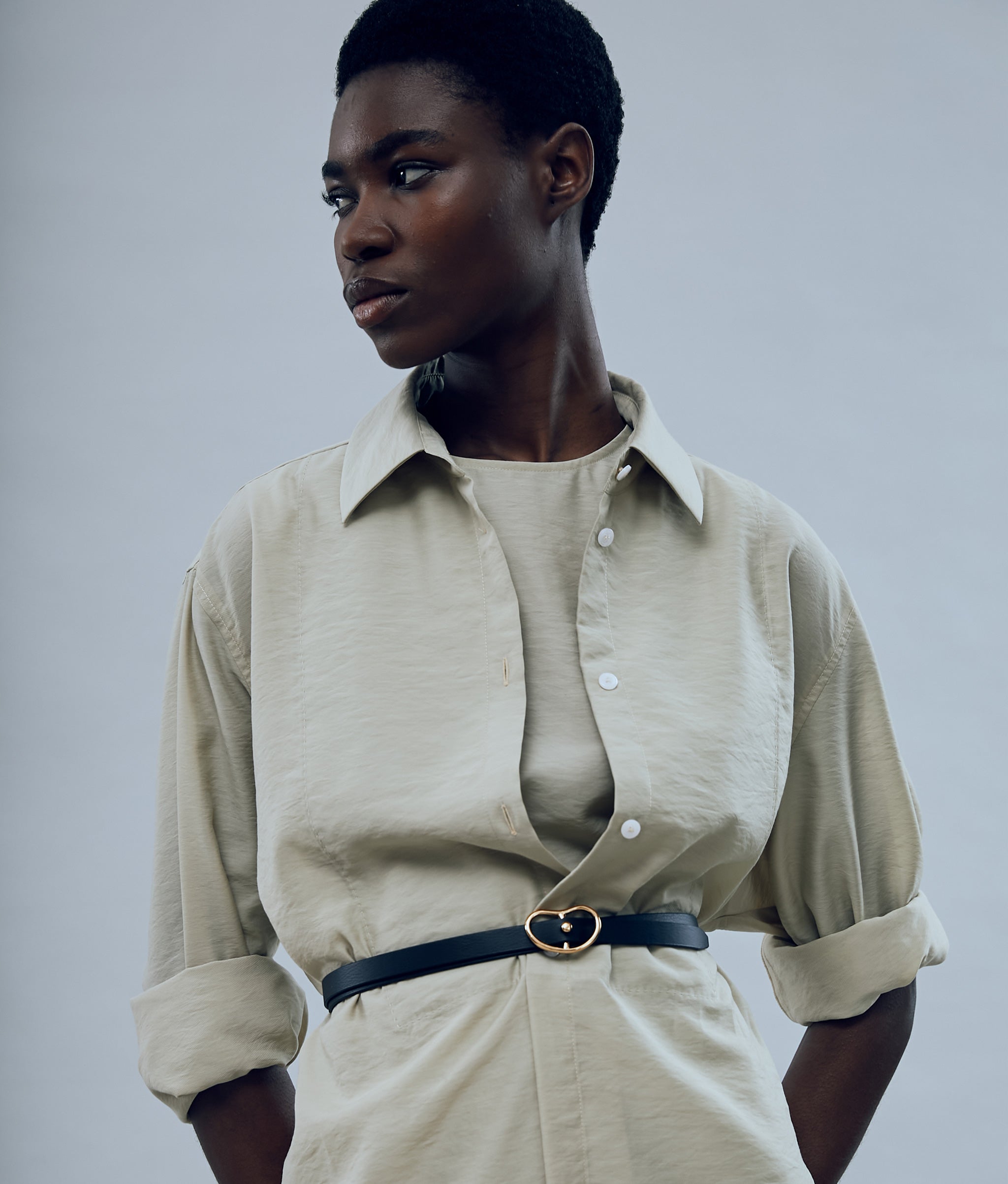 Model on grey backdrop wears tan button-down with Skinny Georgia Belt in Black, alt view.