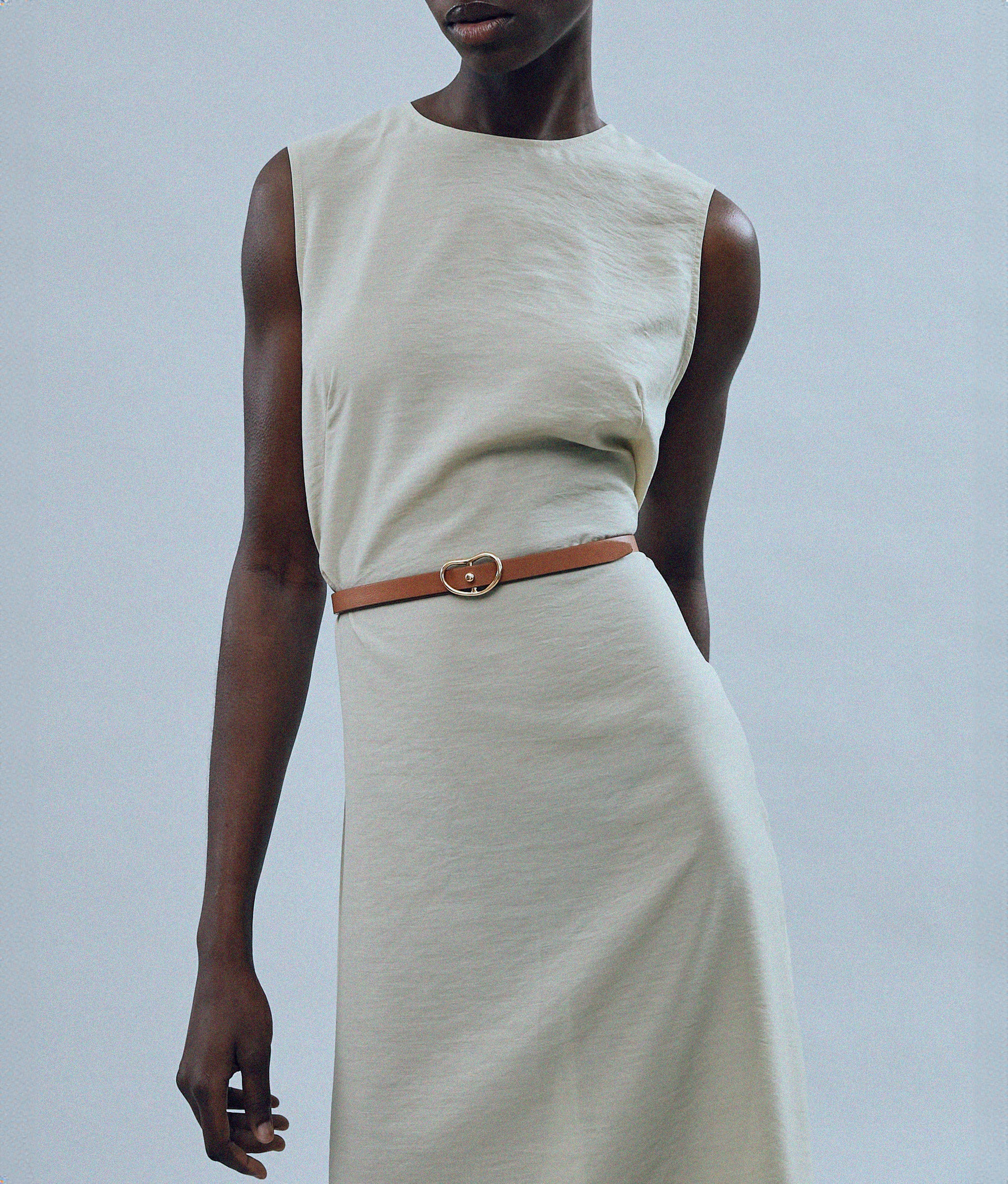 Model on grey backdrop wears tan dress with Skinny Georgia Belt in Tan.