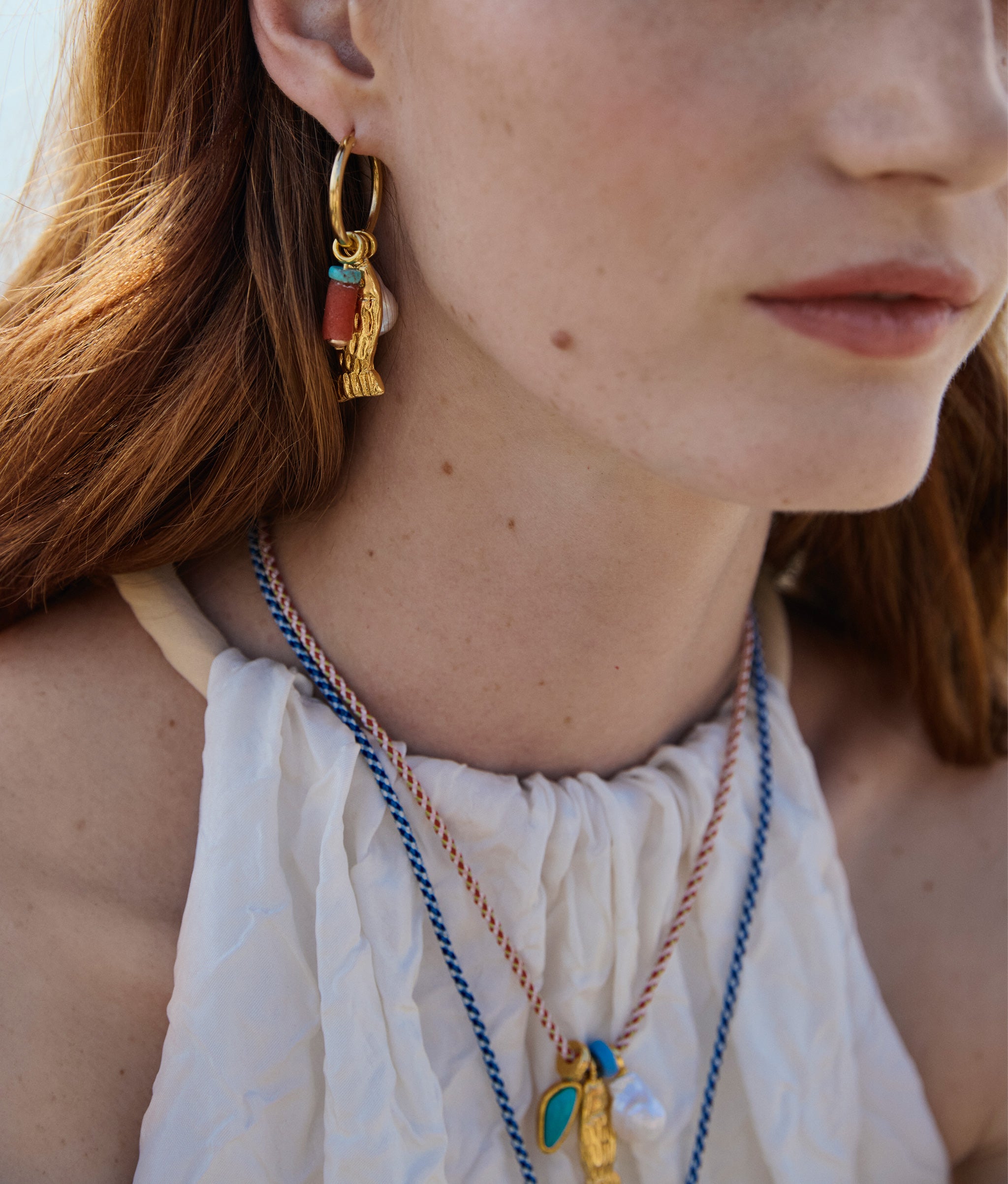 Close up of Model wearing a white blouse, Minnow Necklaces in Ultramarine and Red Hot, and Minnow Hoop Earrings.