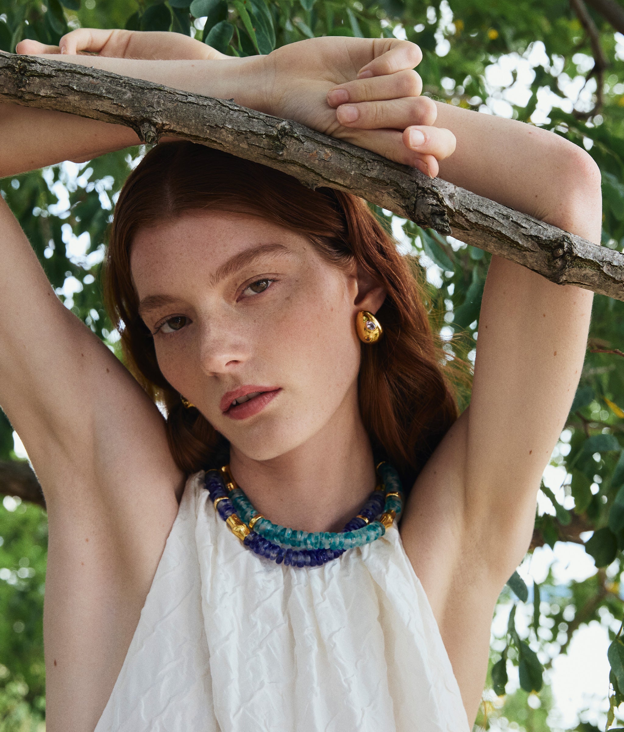 Model poses on tree wearing Toga Beach Necklaces in Dark Blue Wave and in Light Marine