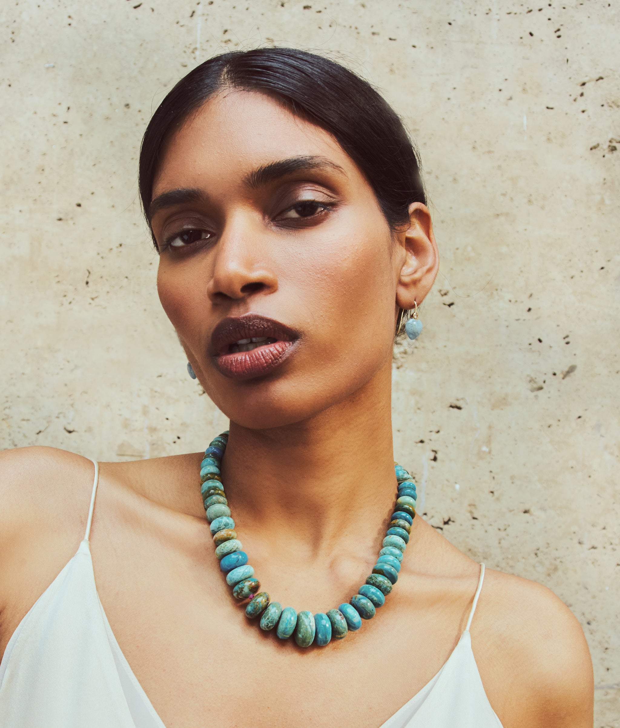 Model wears Large Peruvian Blue Opal, Pink Sapphire & 14k Gold Necklace and Gold Amor Earrings in Diamond & Aquamarine.