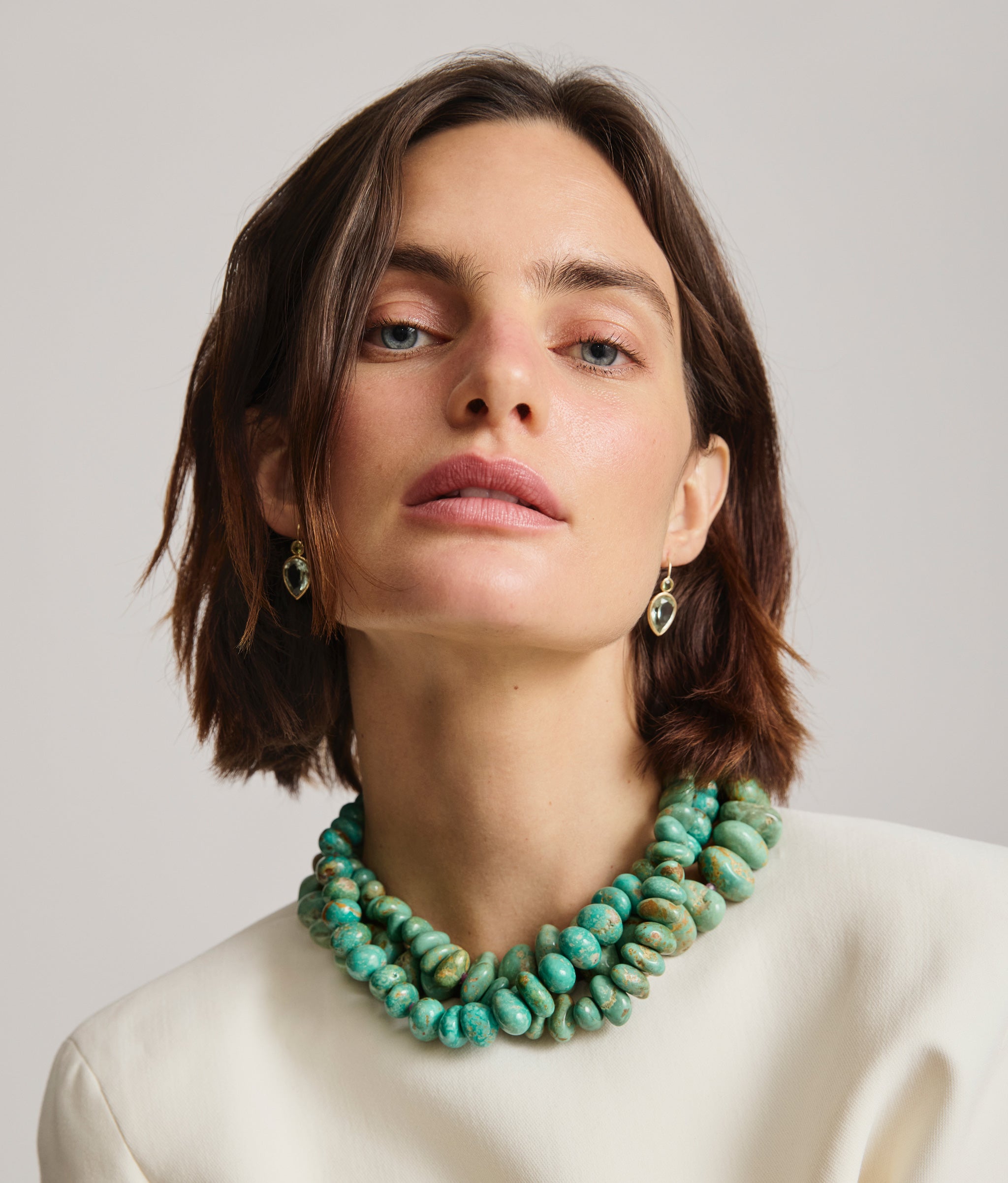 Model wears a stack of Turquoise necklaces and Gold Hera Earrings in Green Amethyst