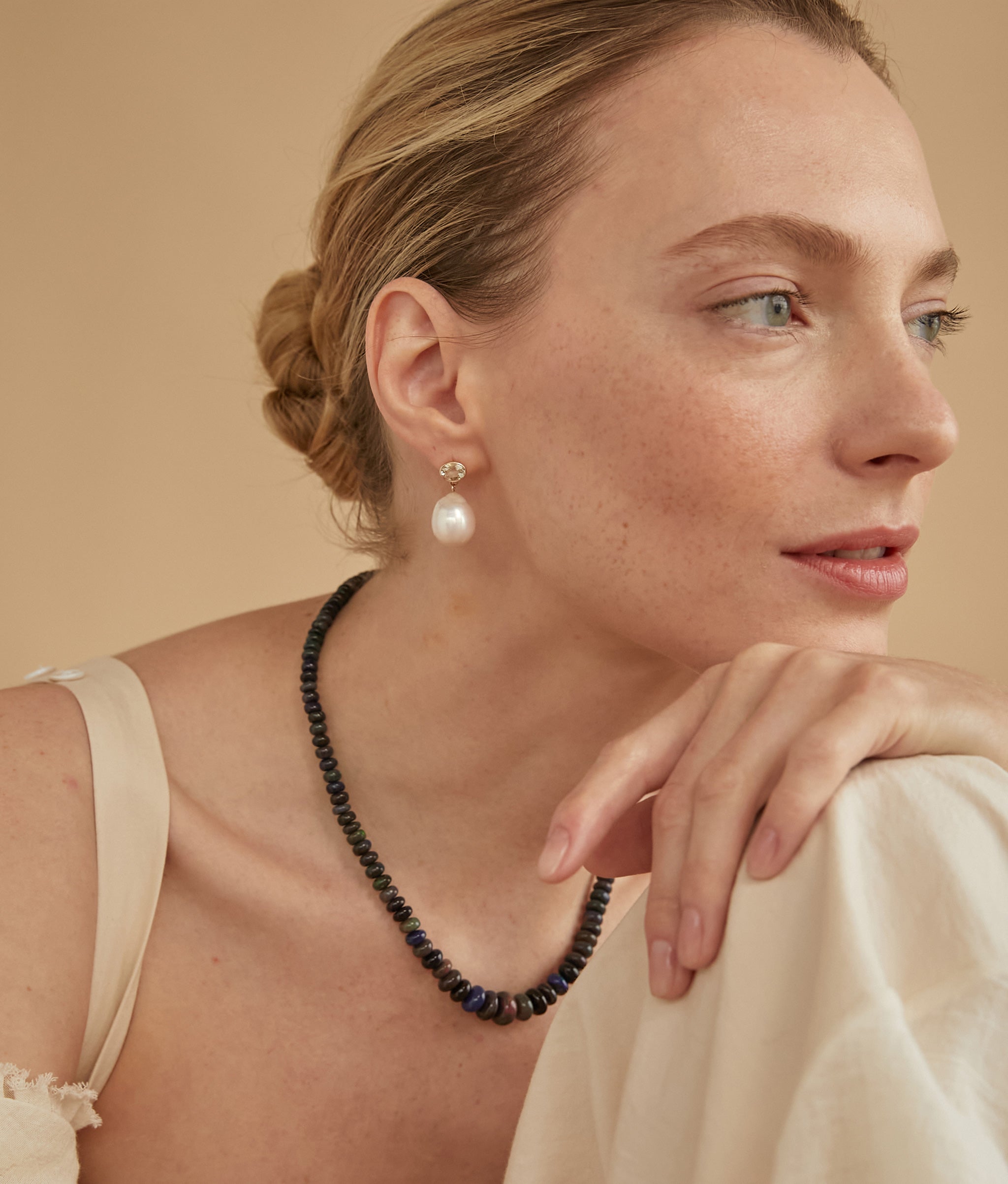Model on tan backdrop wears cream strappy dress and Black Opal and 14k Gold Necklace.