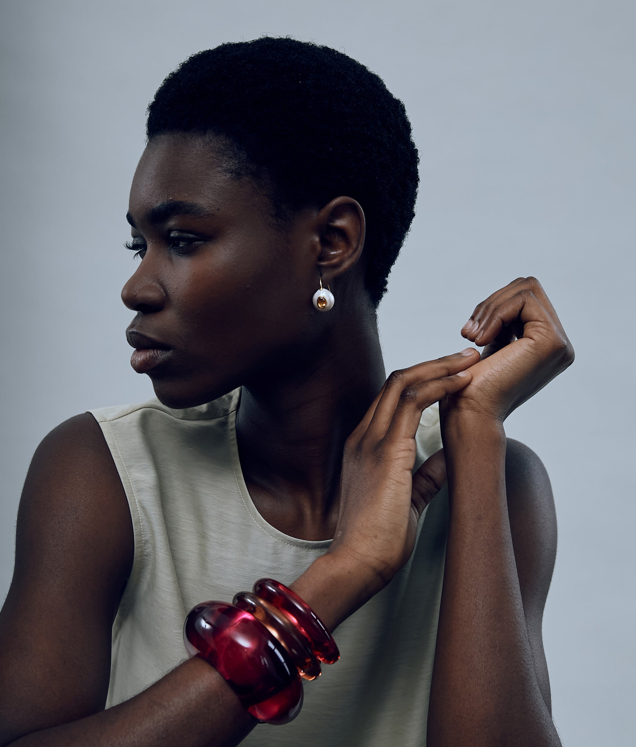 Model on grey background wearing Pearl Pablo Earrings in Citrine paired with Arc and Ridge Cuffs in Magenta and Persimmon.