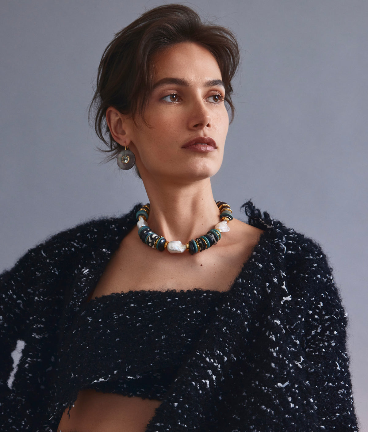 Model on grey backdrop wears black textured outfit with Aquarius Collar and Taj II Earrings.