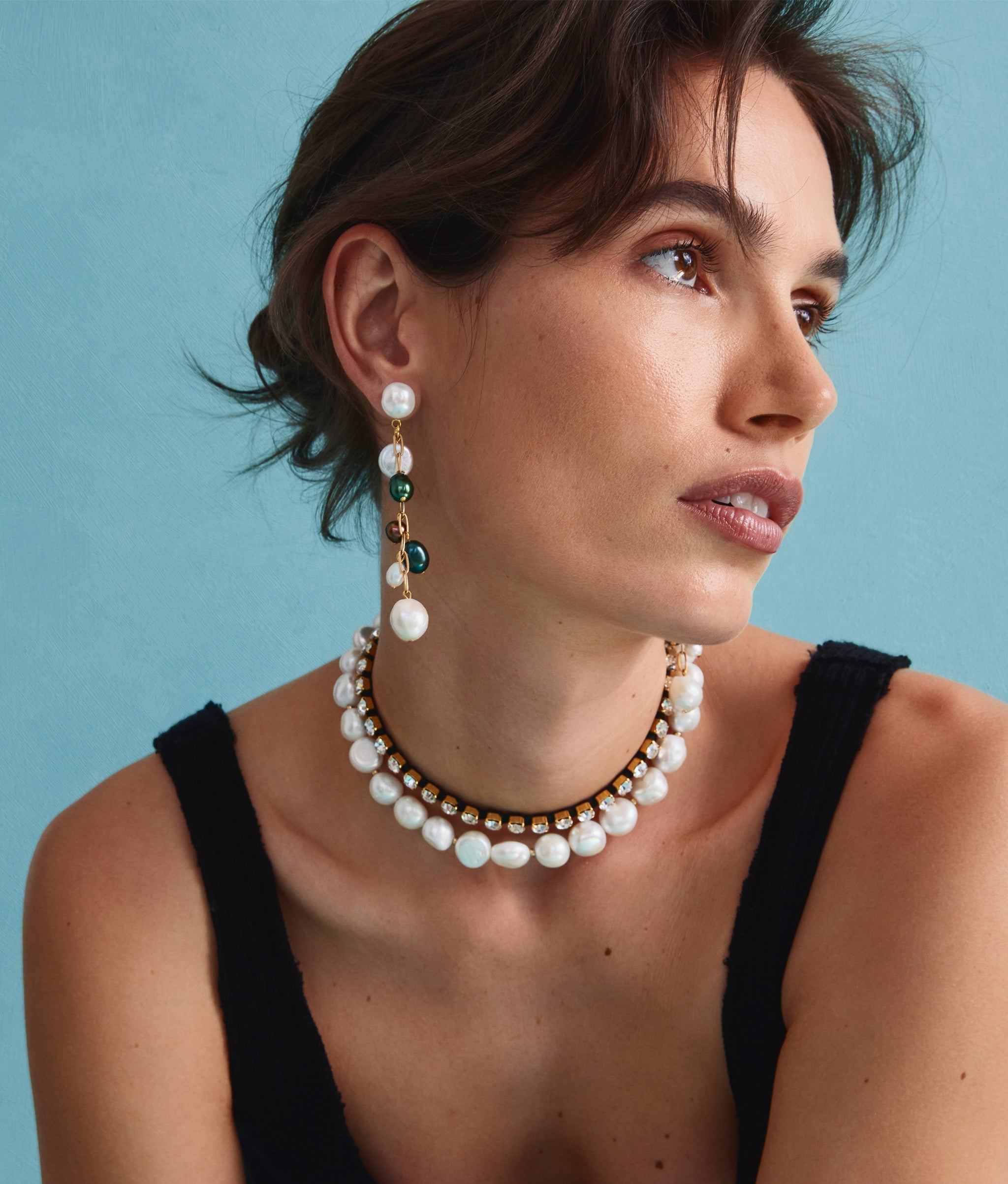 Model on blue backdrop wears black top with Crystal Lagoon II Necklace and Lightning Field Earrings.
