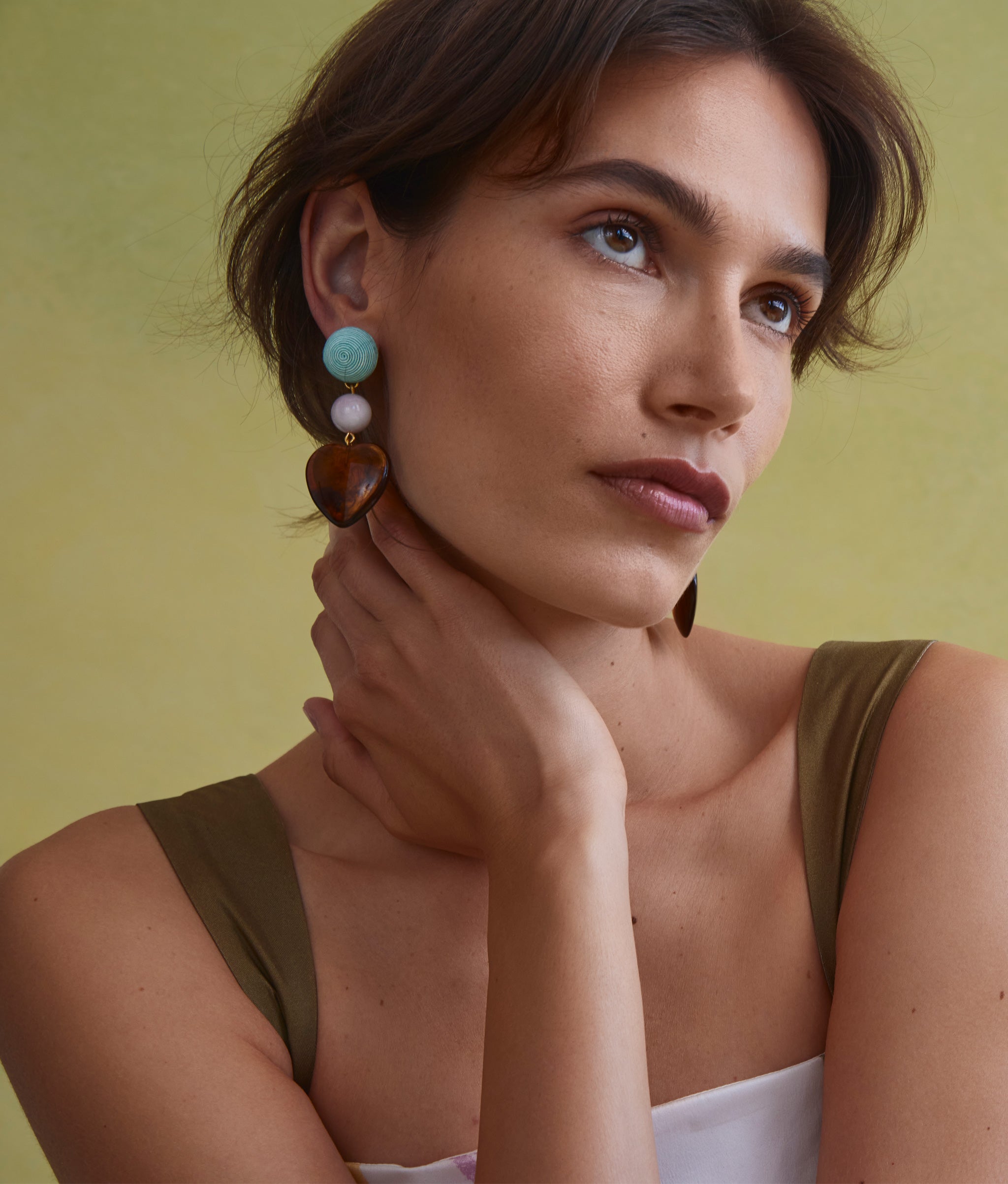 Model on green backdrop rests her hand on her neck and wears the Long Weekend Earrings.
