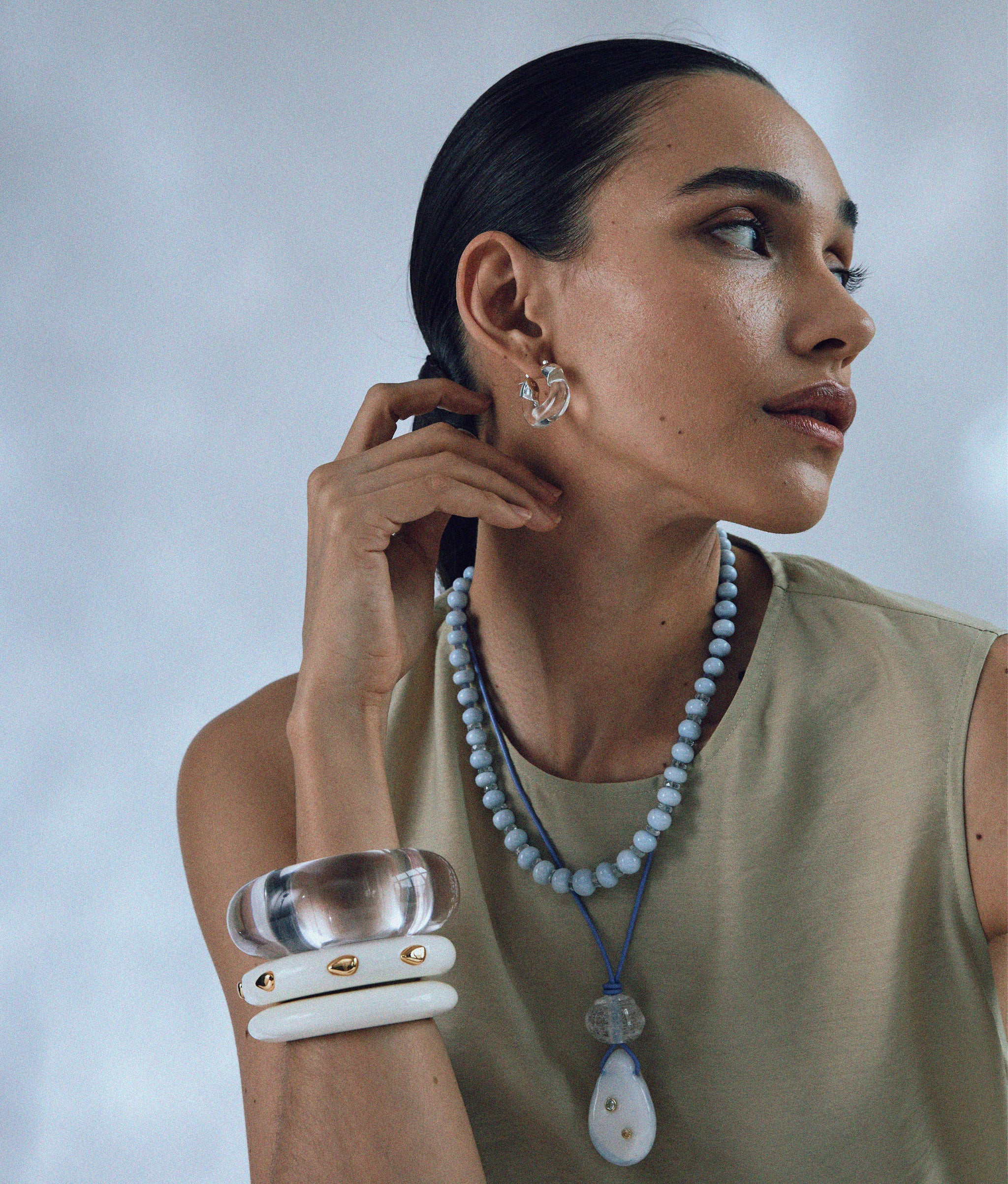 Model in tan top wears Mini Organic Hoops in Silver & Clear with assorted necklaces and cuffs.