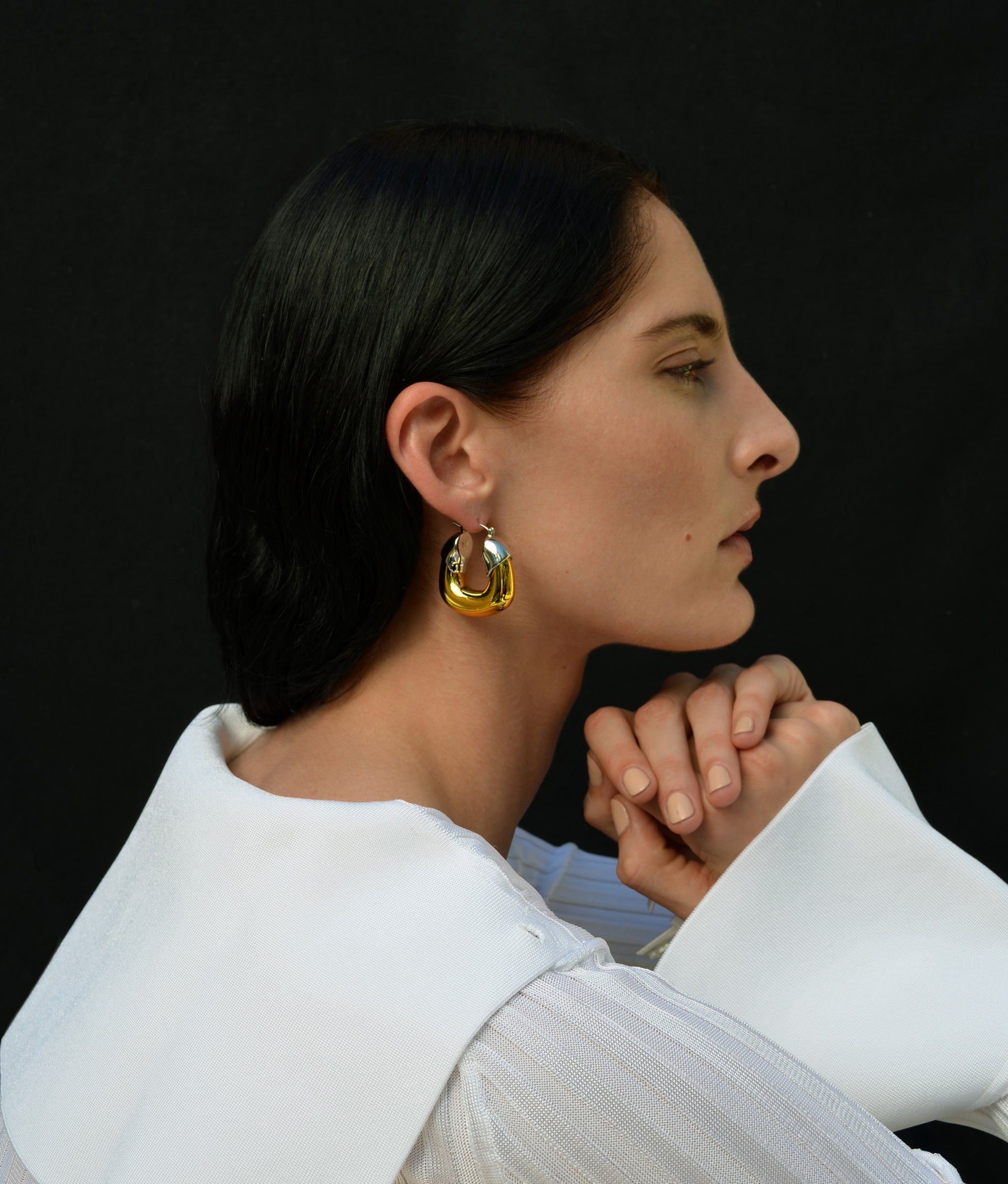 Model in profile on black backdrop wears white blouse and Organic Hoops in Mixed Metal.