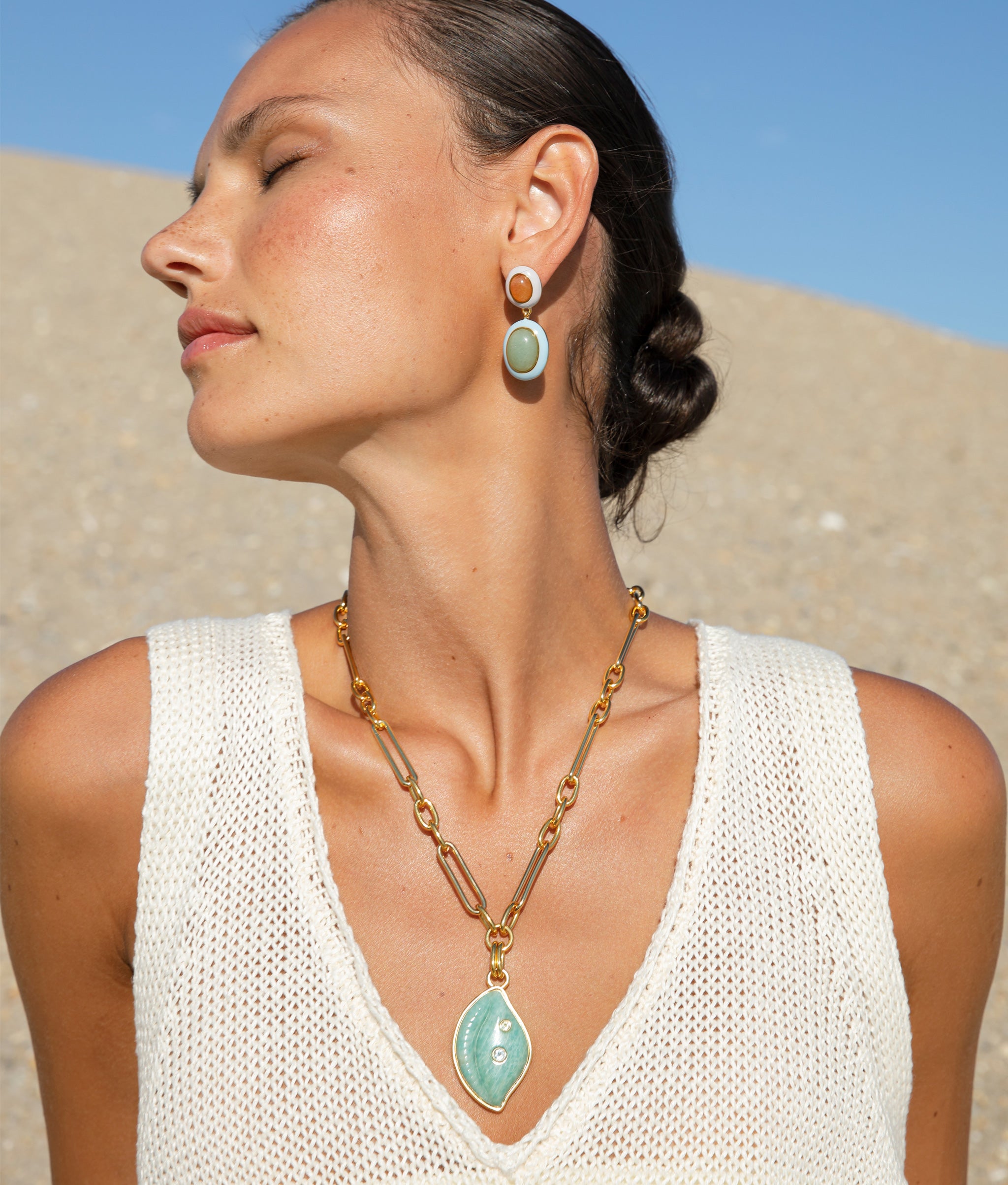 Close up of model on the beach wearing the Papaya Earrings paired with the Cowrie Shell Necklace in Amazonite.