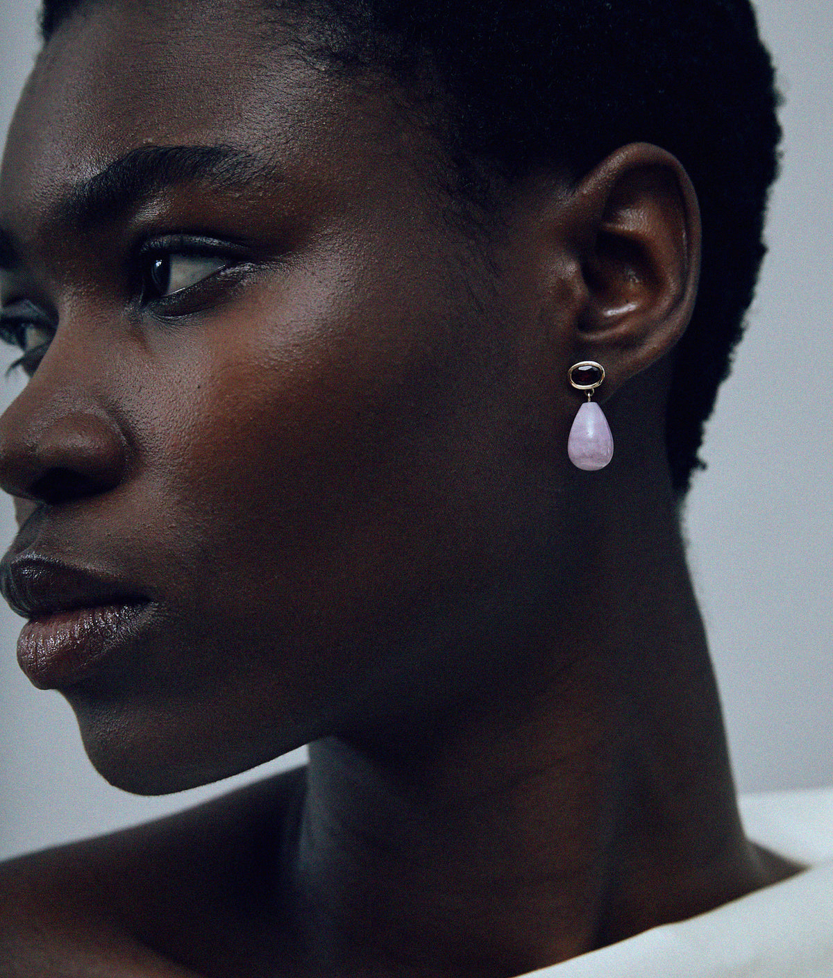 Close-up of model on grey background wearing the 14k Gold Drop Earrings in Garnet & Kunzite. nzite.