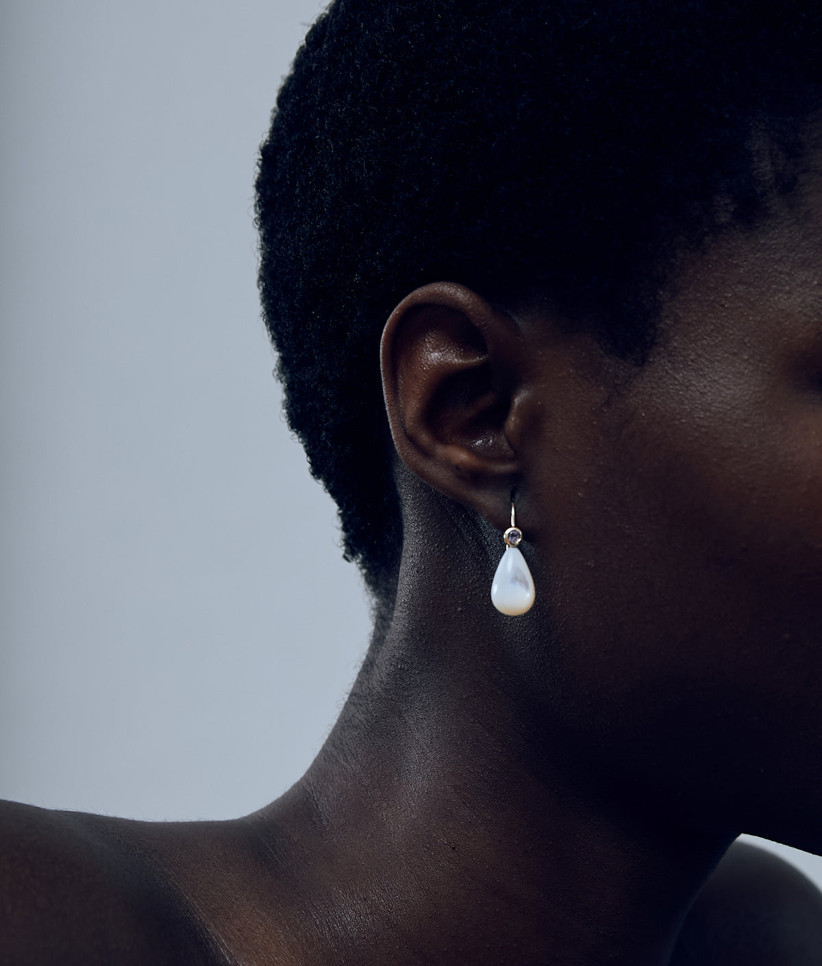 Close-up of model on grey background wearing the 14k Gold Drop Earrings in Pink Amethyst & Pearl.