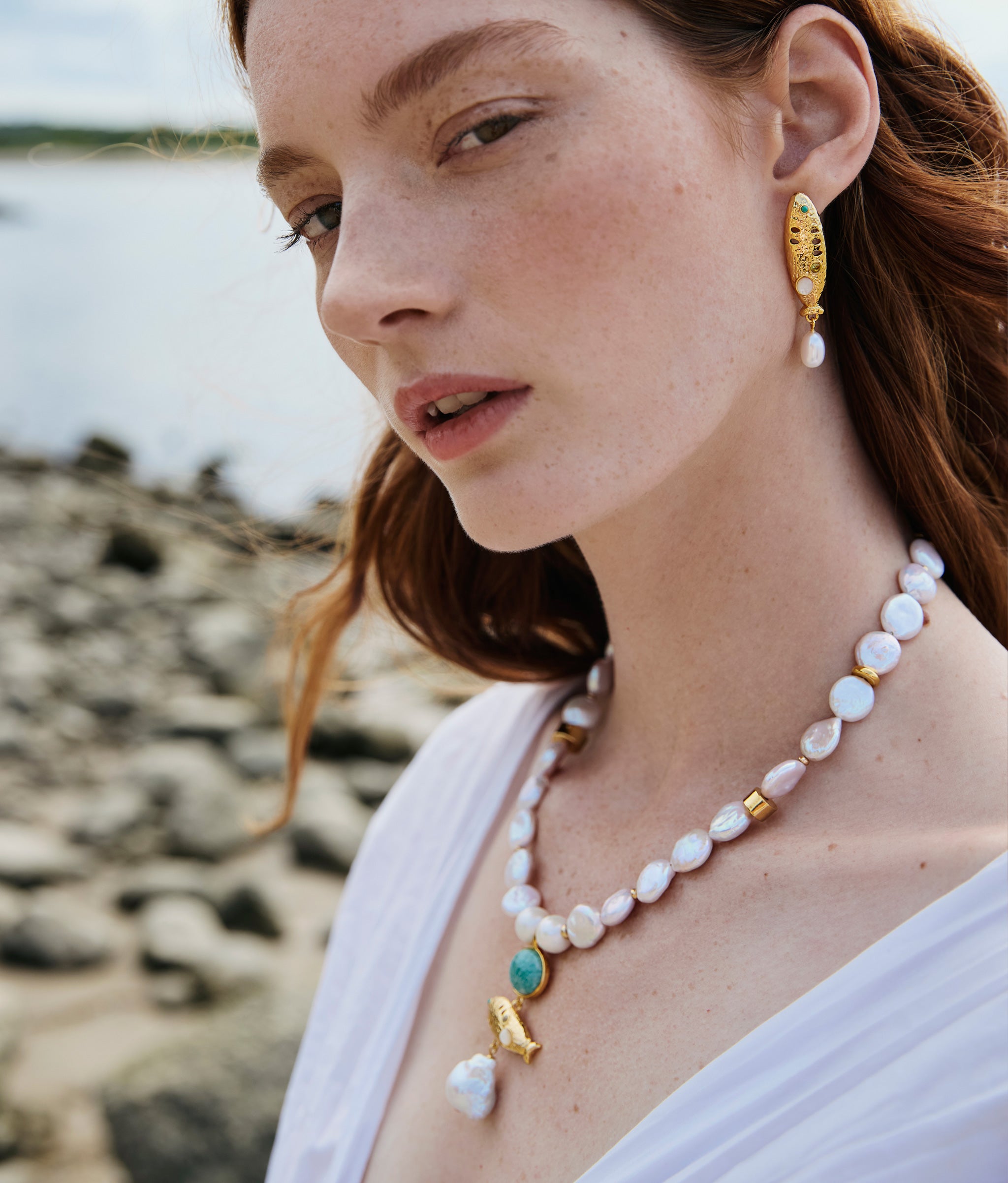Model at rocky water wears Sardinia Pearl Necklace and Sardinia Pearl Earrings.