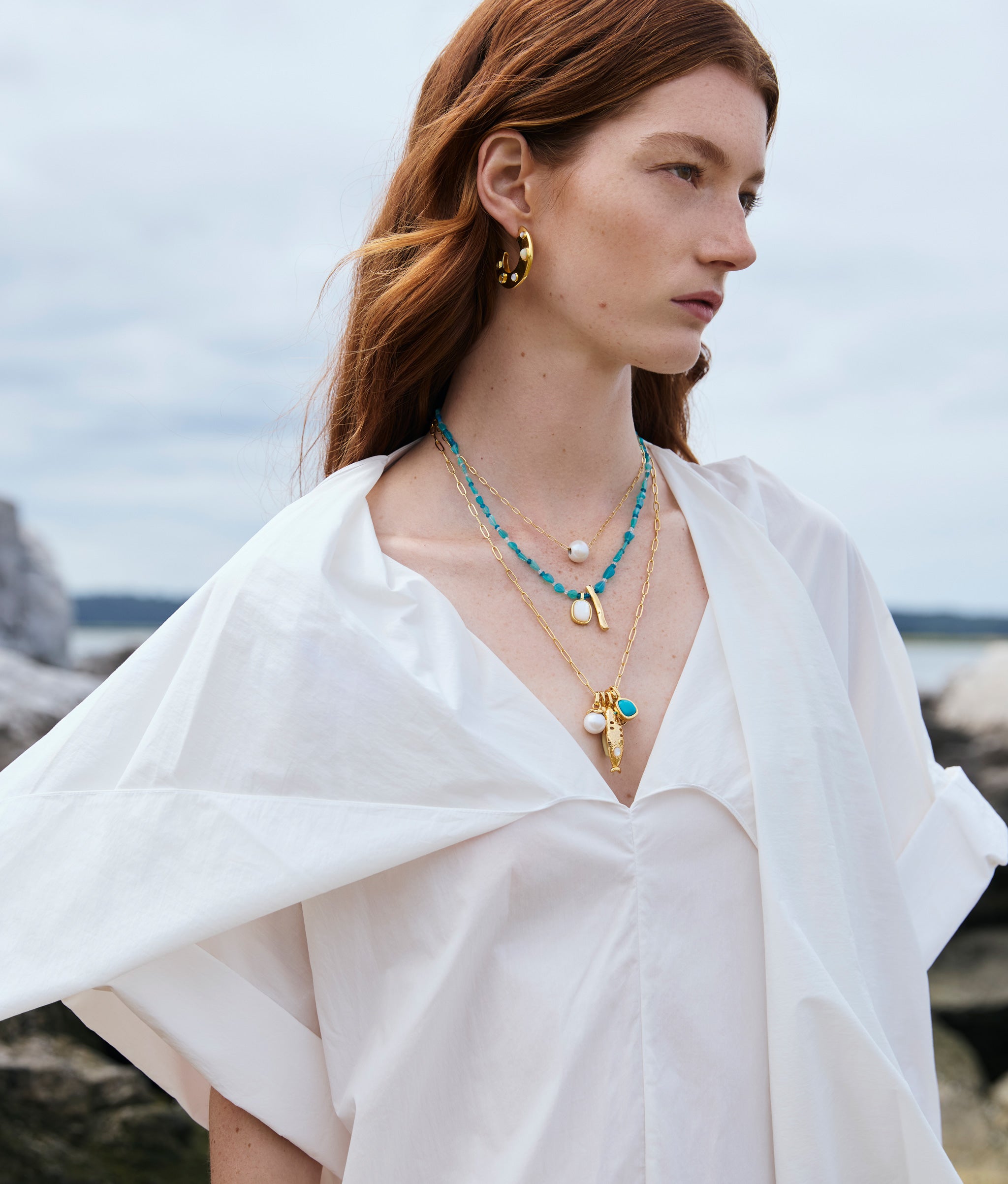 Model in white dress wears Saucer Hoops in Dotted Pearl, Sardinia Charm Necklace, and Miyako Necklace