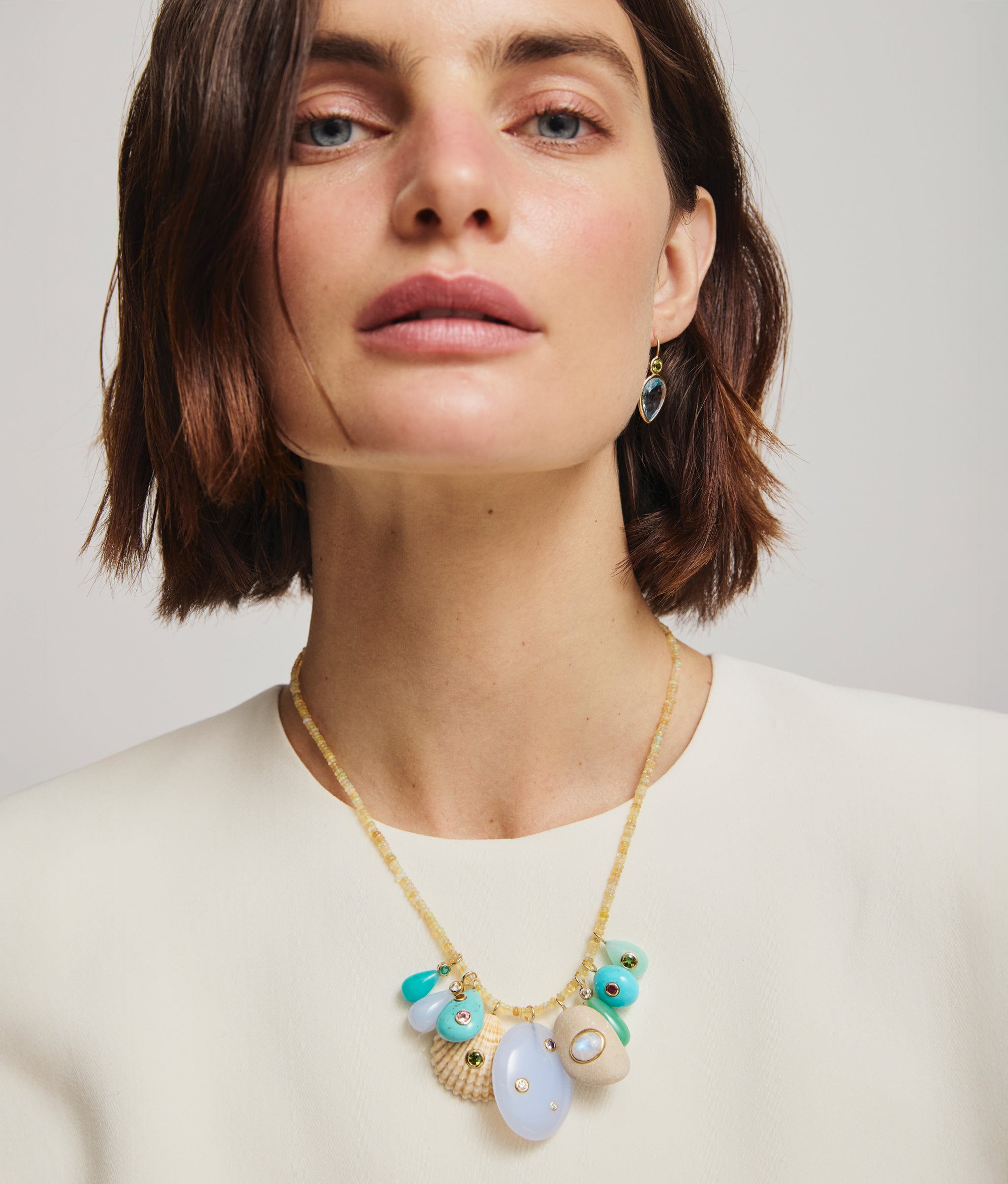 Model in cream top wears opal bead necklace with assorted semiprecious and shell charms.