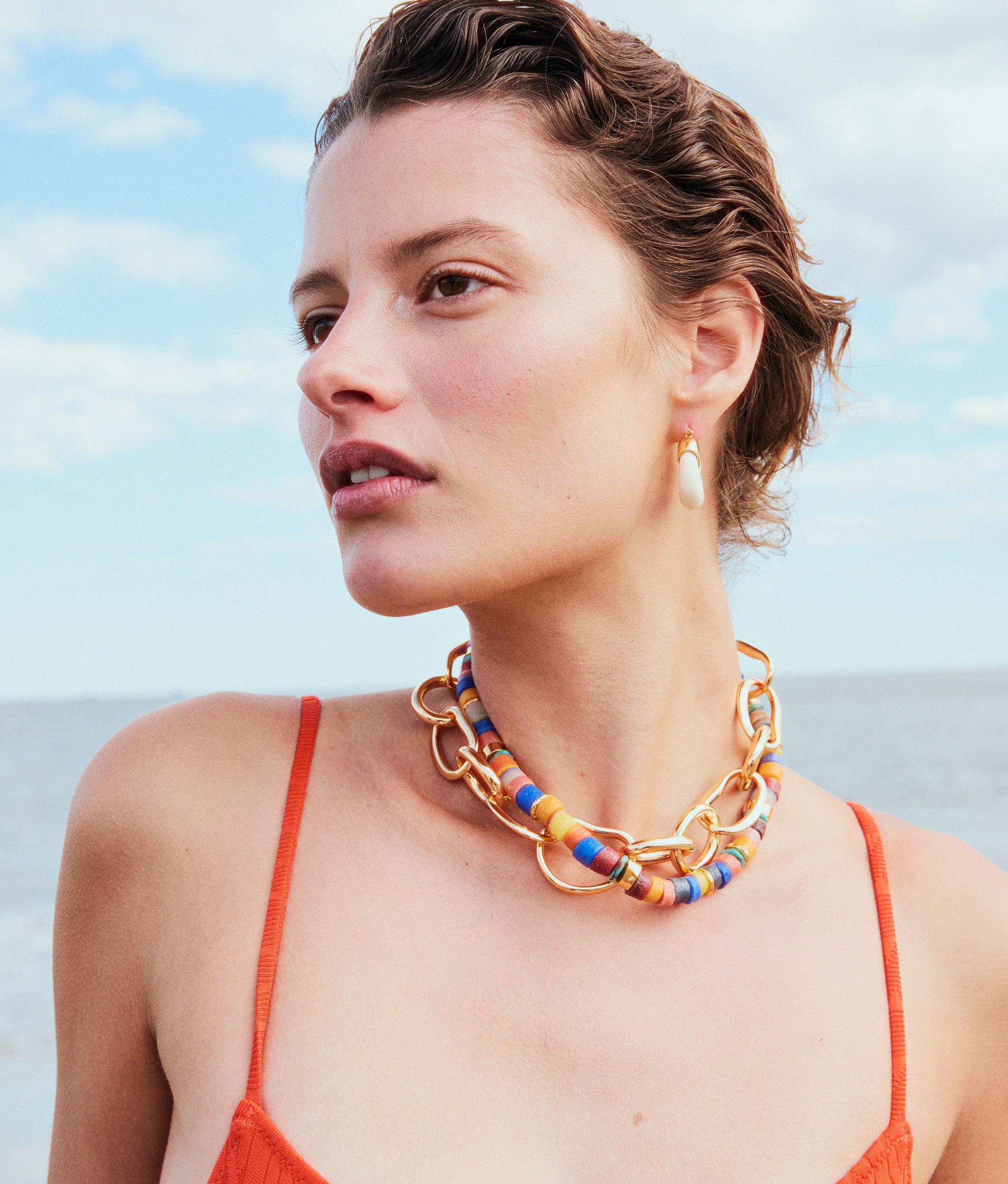 Model on beach wears red swimsuit with Lido Necklace, Porto Chain in Gold and Mini Organic Hoops in Alabaster