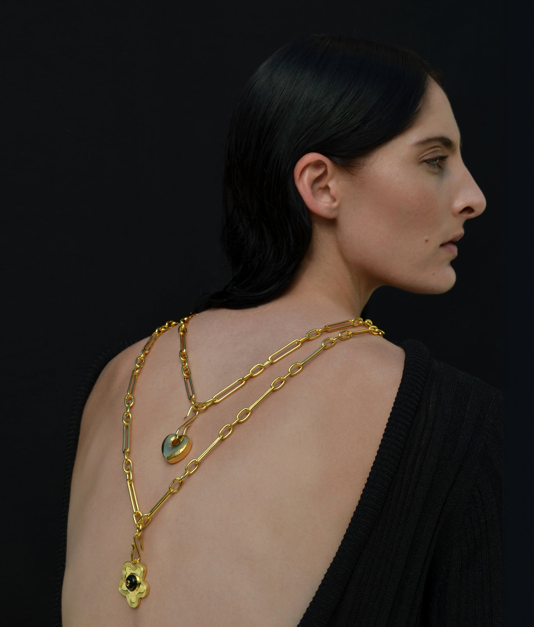 Model on black backdrop wears two gold necklaces backwards, with Nana Pendant and Golden Love charms.