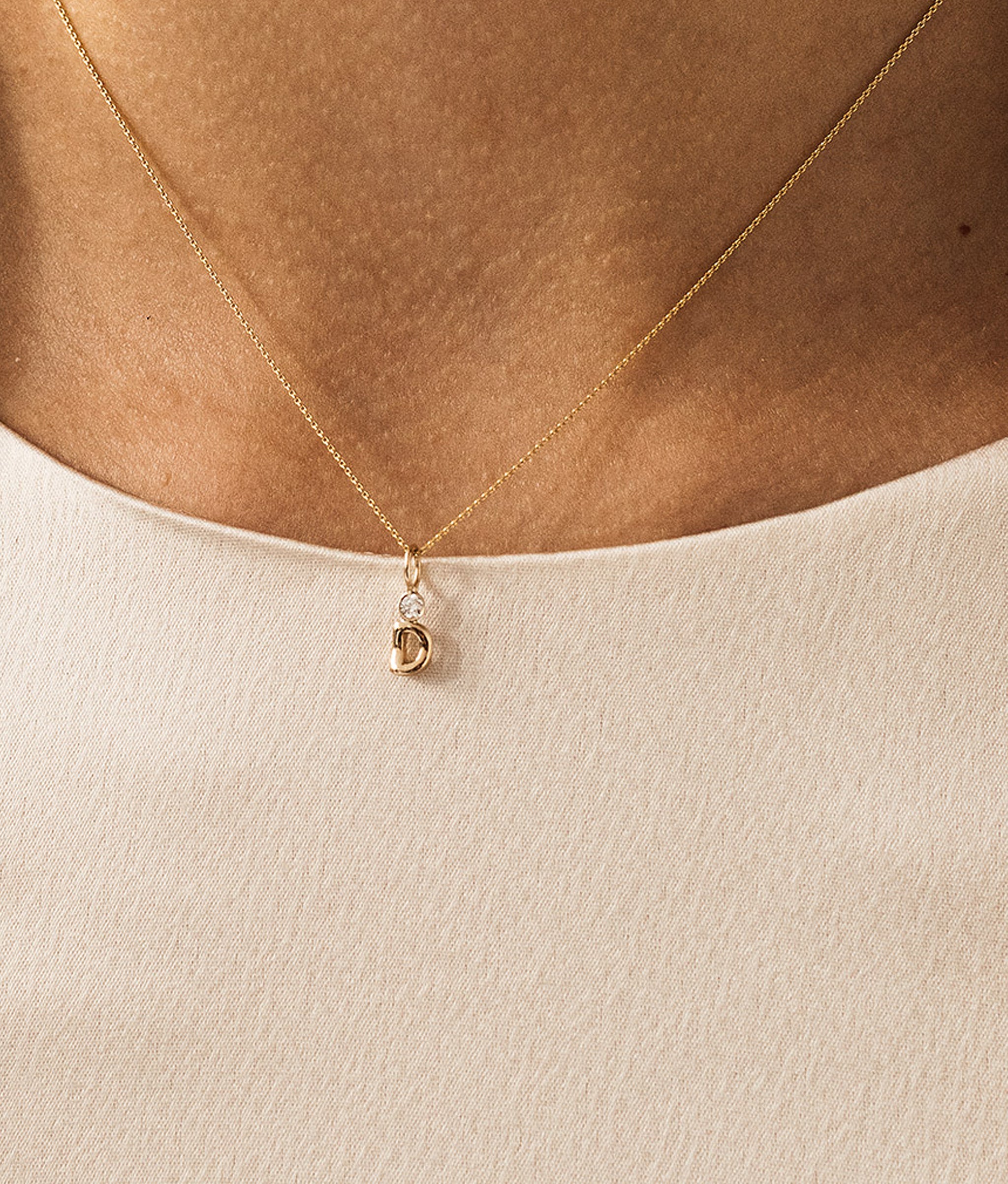 Model's neck in cream top wearing delicate fine gold chain with Alphabet Soup letter Charm.