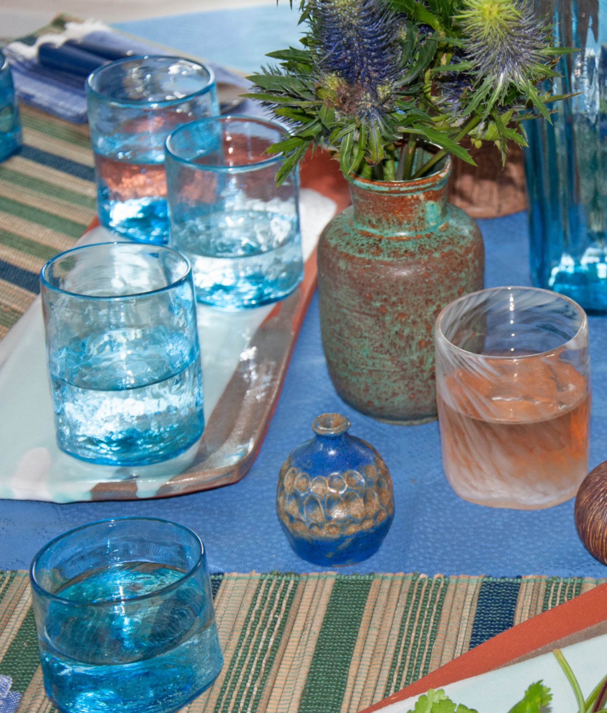 Blue and green tablescape with placemats, glasses, vintage vases and Vaso in New White.