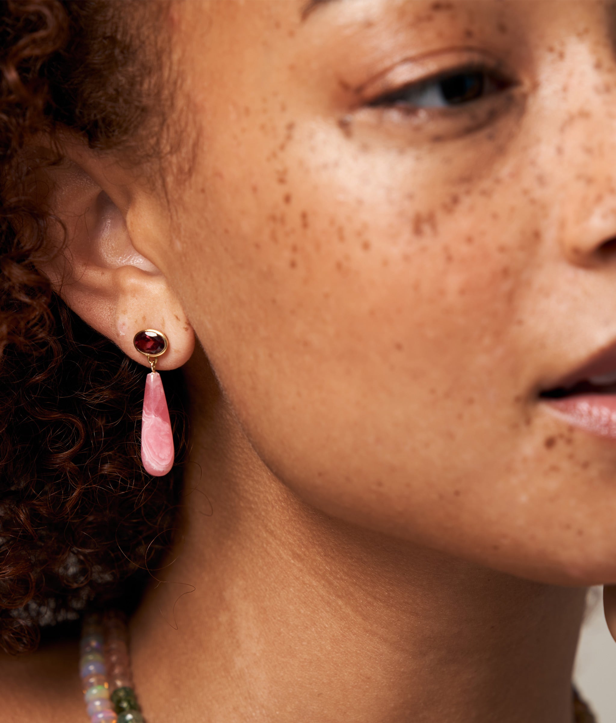 On model side profile 14k gold earrings with semiprecious garnet tops and hanging pink rhodochrosite drops.