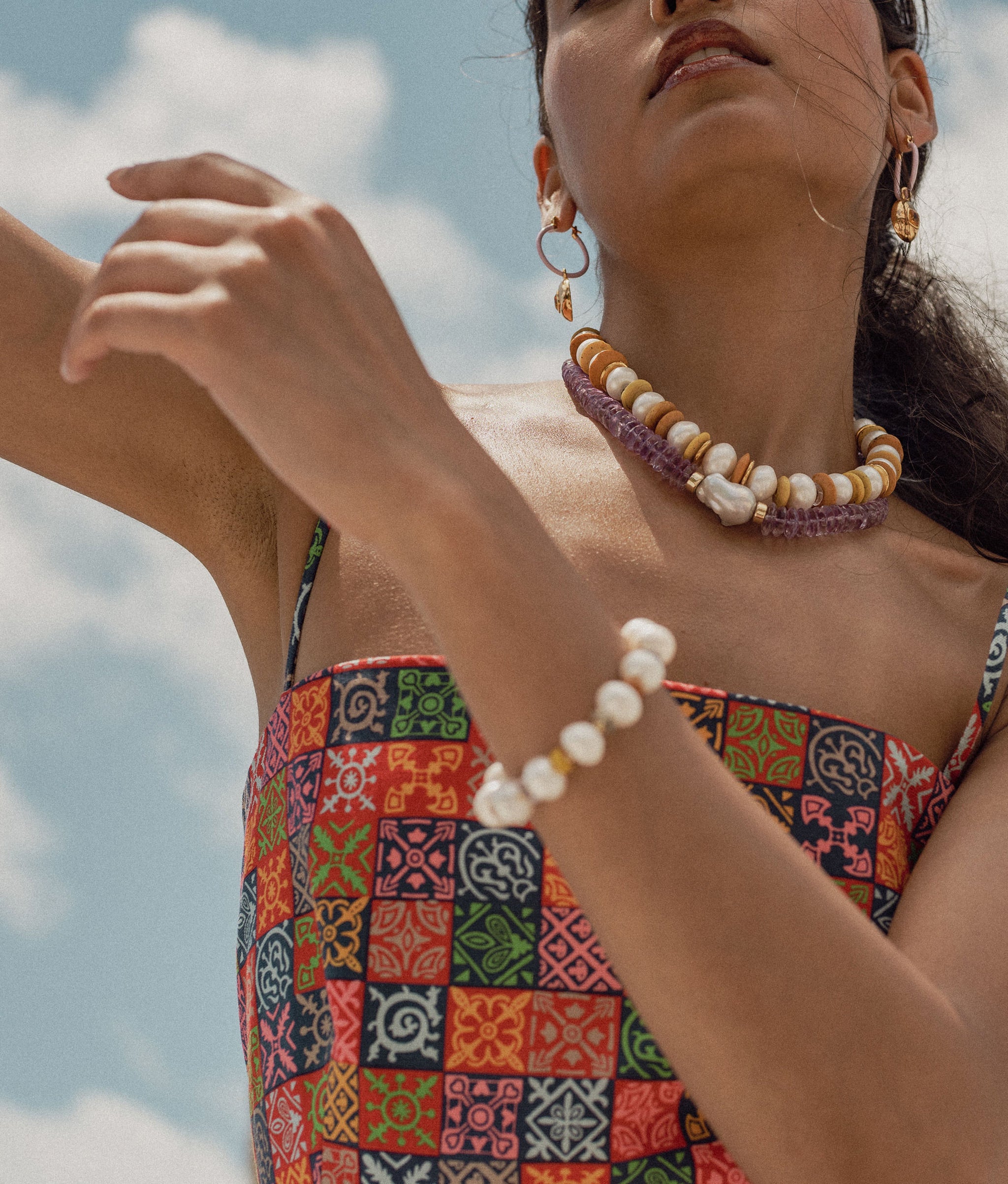 Model in printed dress against blue sky wears Sunlight Bracelet and Necklace