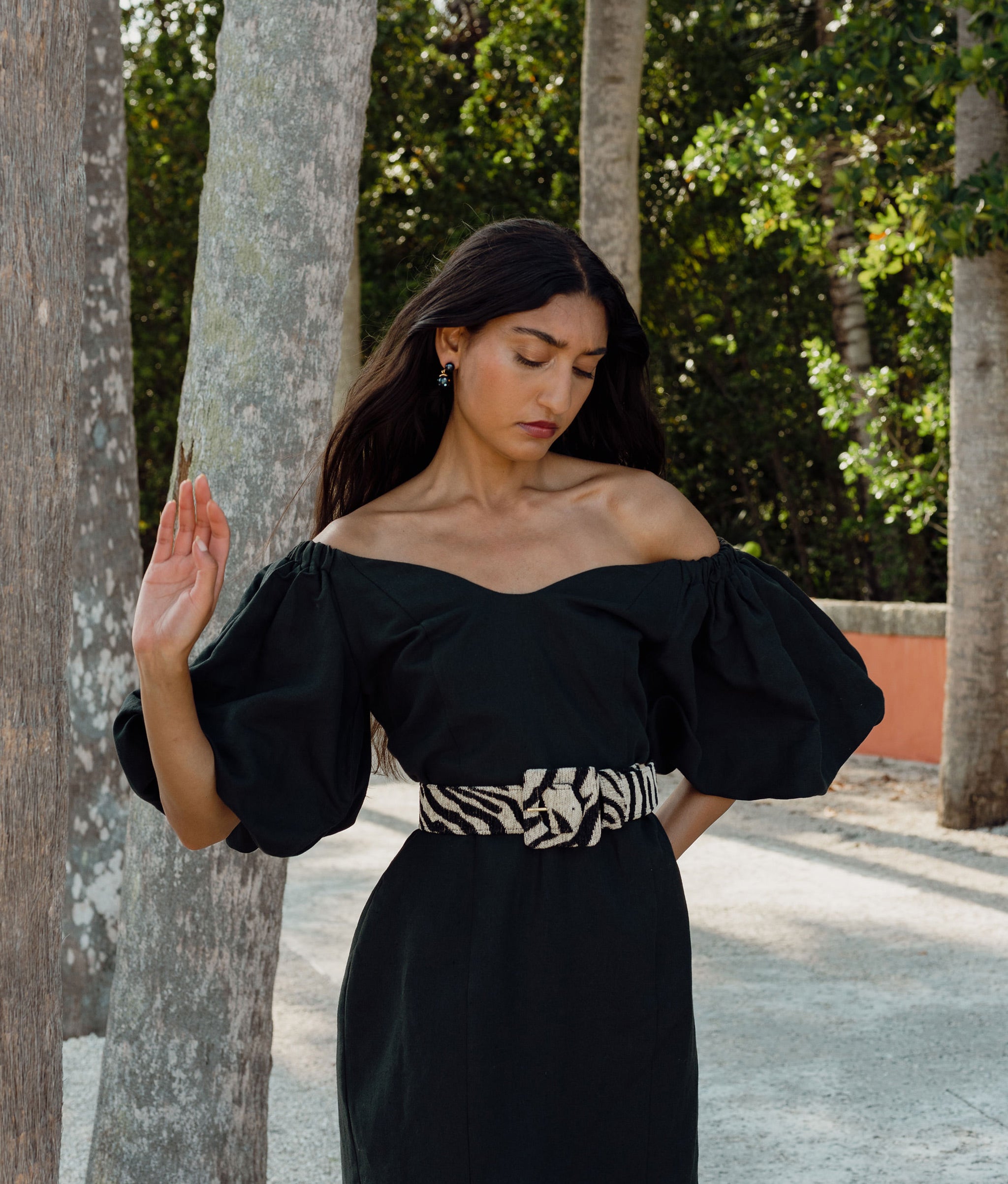 Model wears black dress with Agnes Belt in Black and White Tiger, walks among tree-lined path.