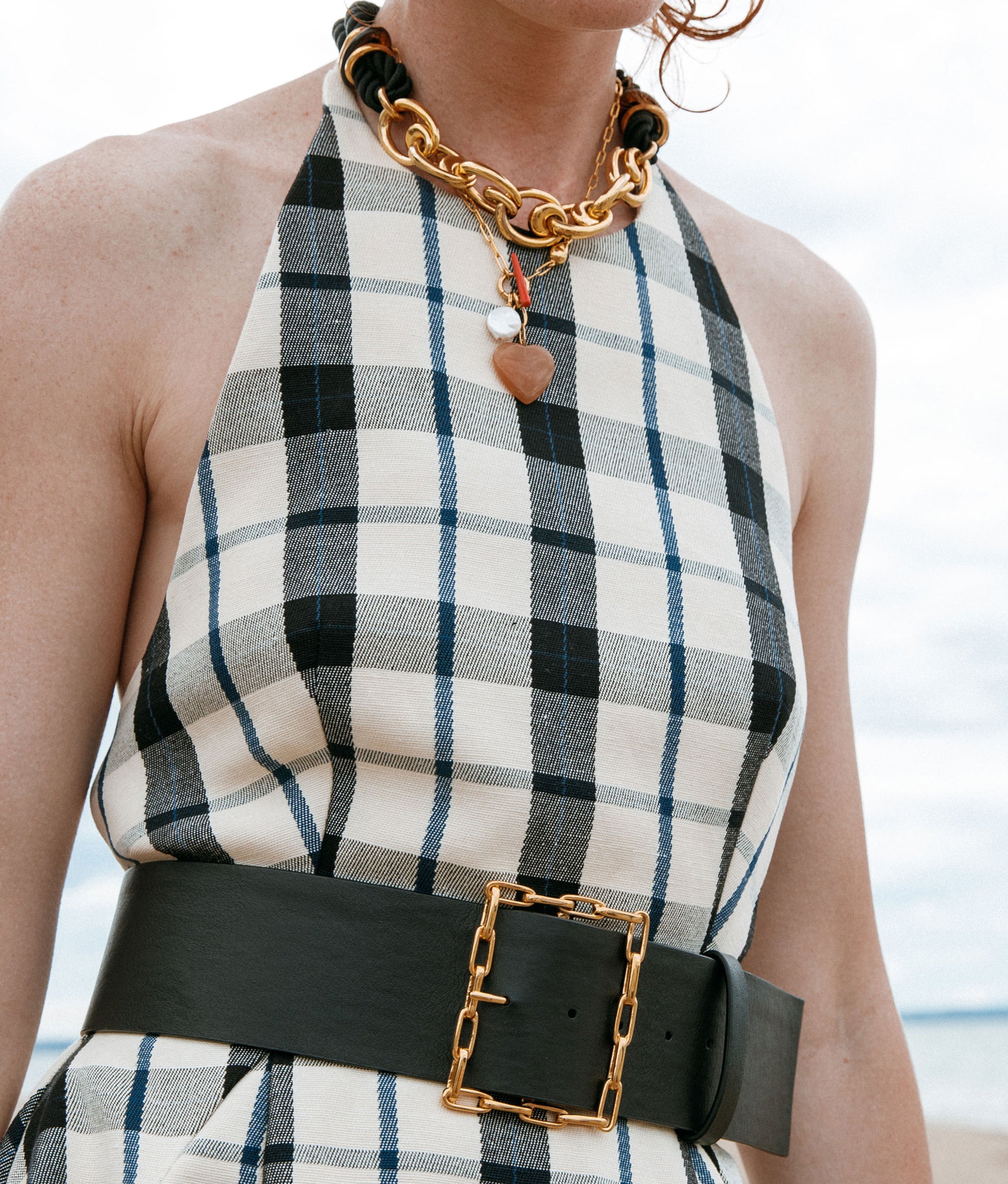 Model in plaid dress wears Geo Chain Belt in Black and assorted necklaces.