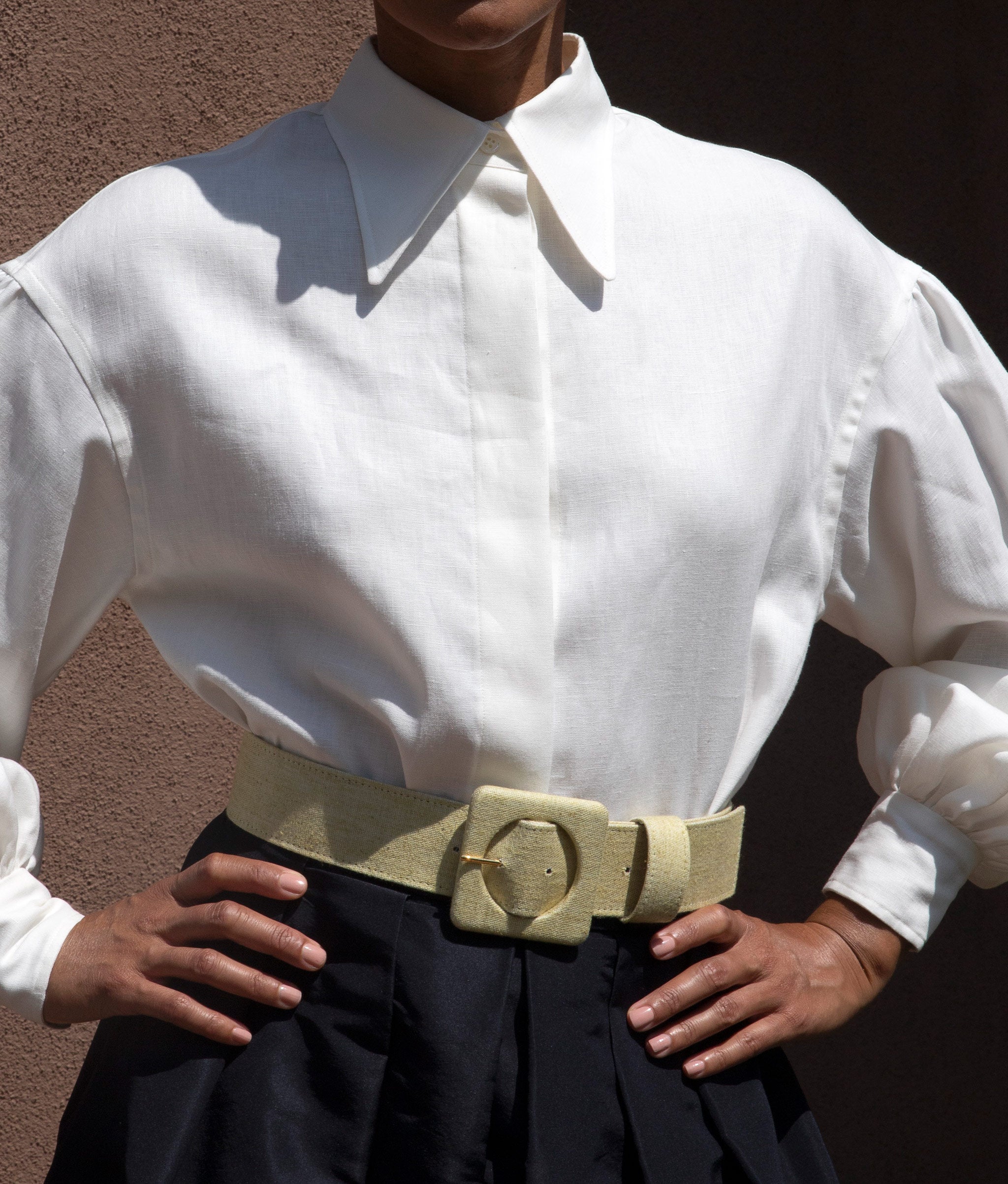 Model with hands on hips wears white blouse, black skirt and Agnes Belt in Citron Twill.