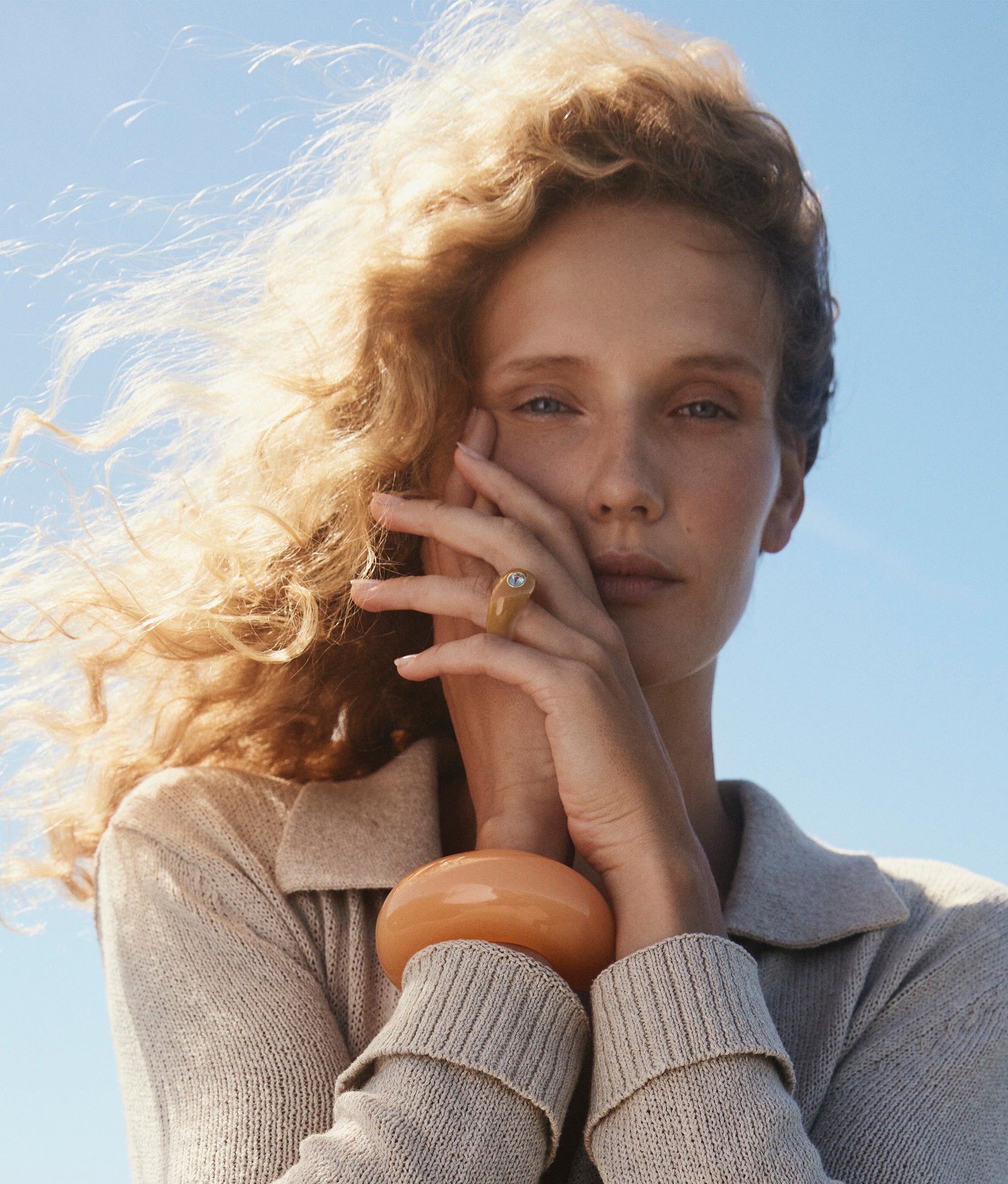 Model on blue wears beige sweater with Monument Ring in Ochre and Arc Cuff in Apricot.