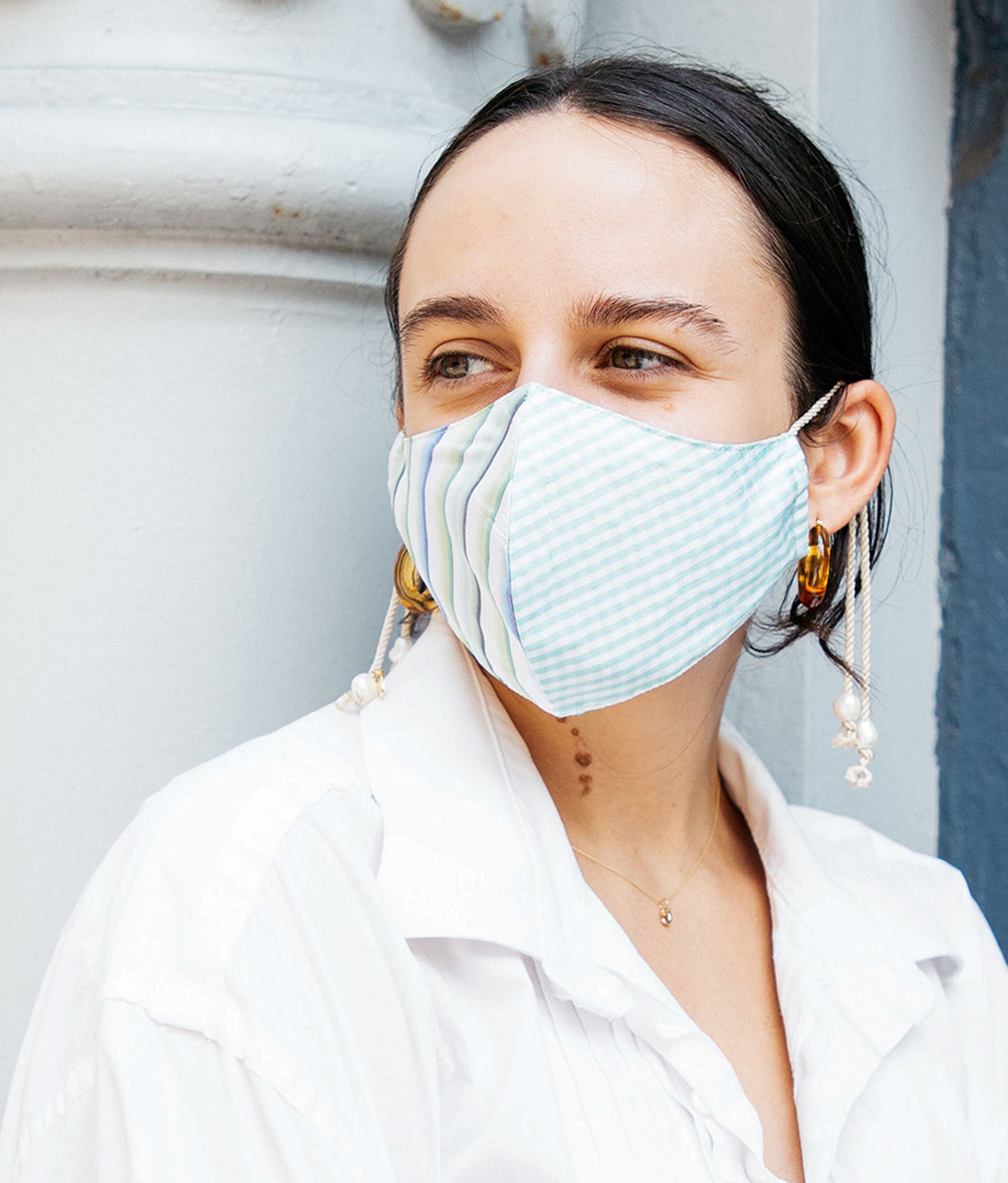Model against blue wall and white column wears white button-down shirt and the Face Mask in Palma.