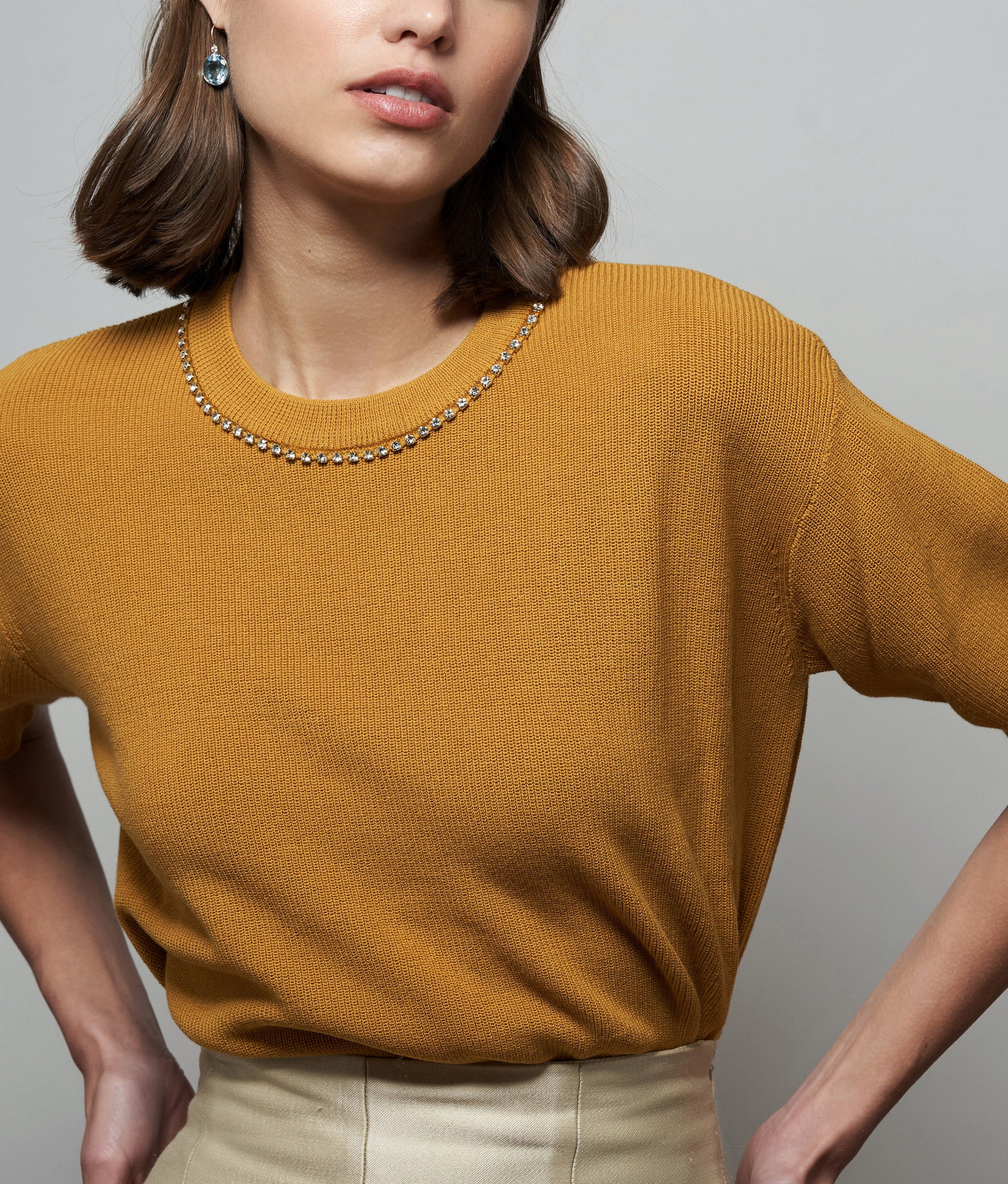 Model on grey backdrop wears Uptown Sweater with Pool Earrings.