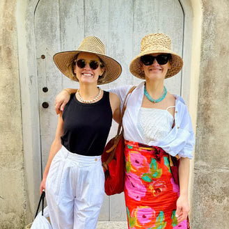 Twins Lizzie and Kathryn Fortunato pose in front of wooden doorway in straw hats and resort wear