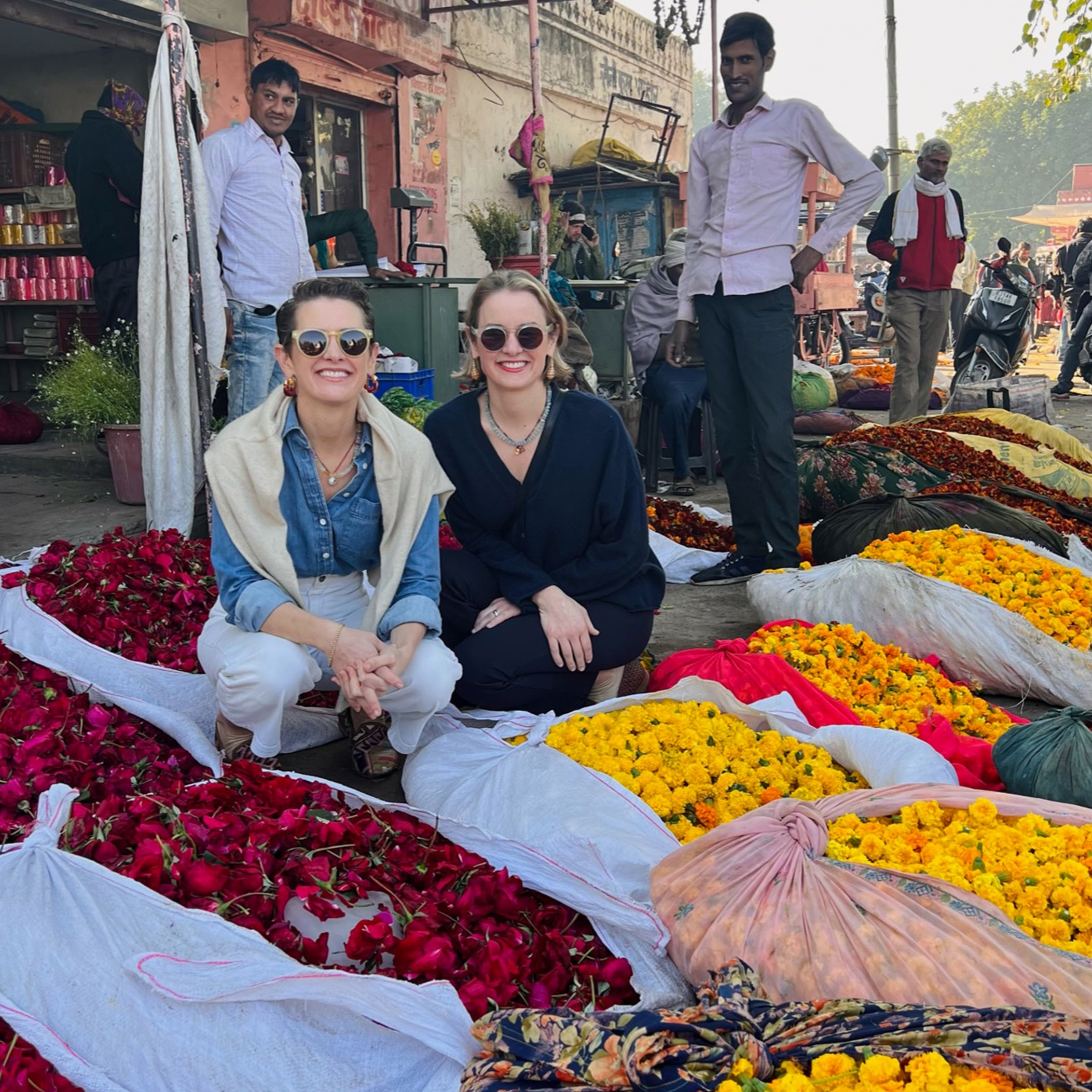 Lizzie and Kathryn pose with bags of colorful flowers at a market in India