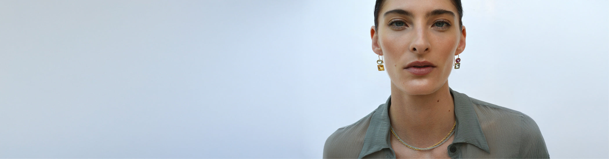 Model on blue background wears sage blouse with Duo Earrings, Aquamarine beaded base and gold chain necklace