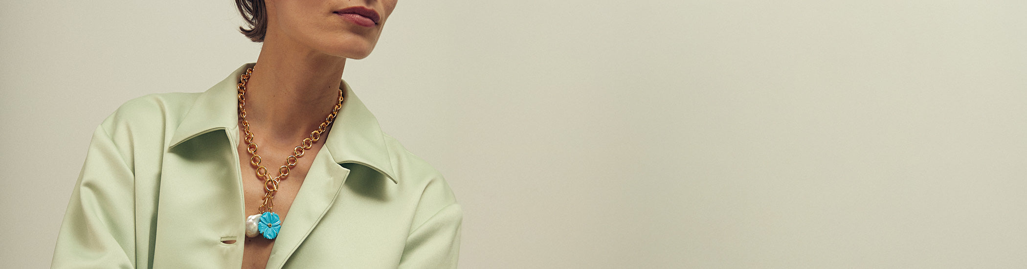 Model on tan backdrop wears light green shirt with Mood Necklace in Gold and New Bloom Charm in Cerulean