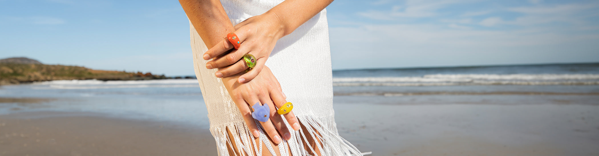 Model on beach with close-up on hands wearing colorful glass rings