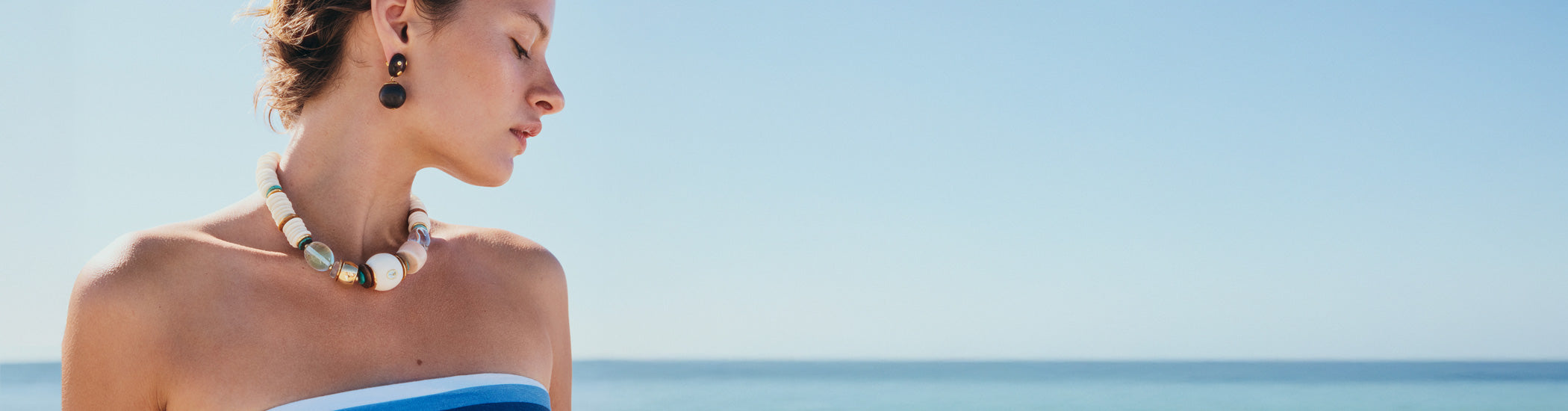 Model on blue sea backdrop wears Coquina Necklace and Nopales Earrings