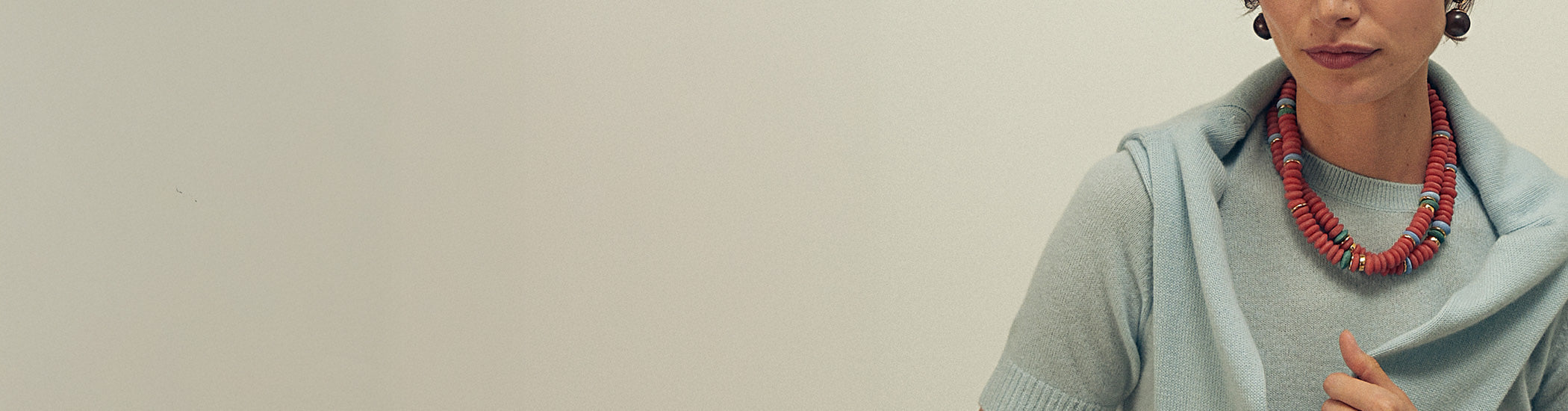 Model on grey backdrop wears blue sweater with two red beaded Laguna Necklaces