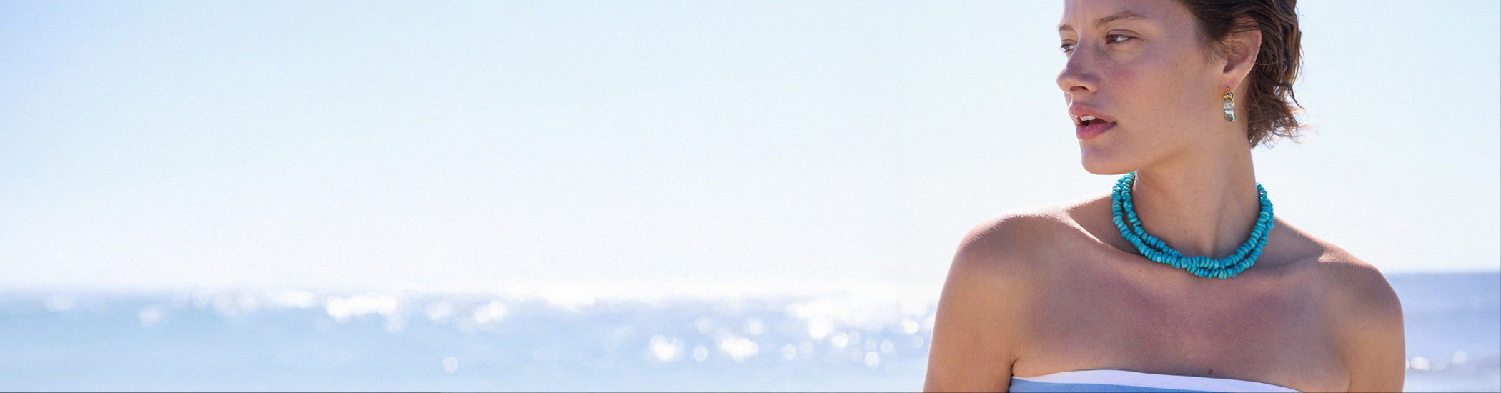 Model against sea backdrop wears tube top and two turquoise bead necklaces
