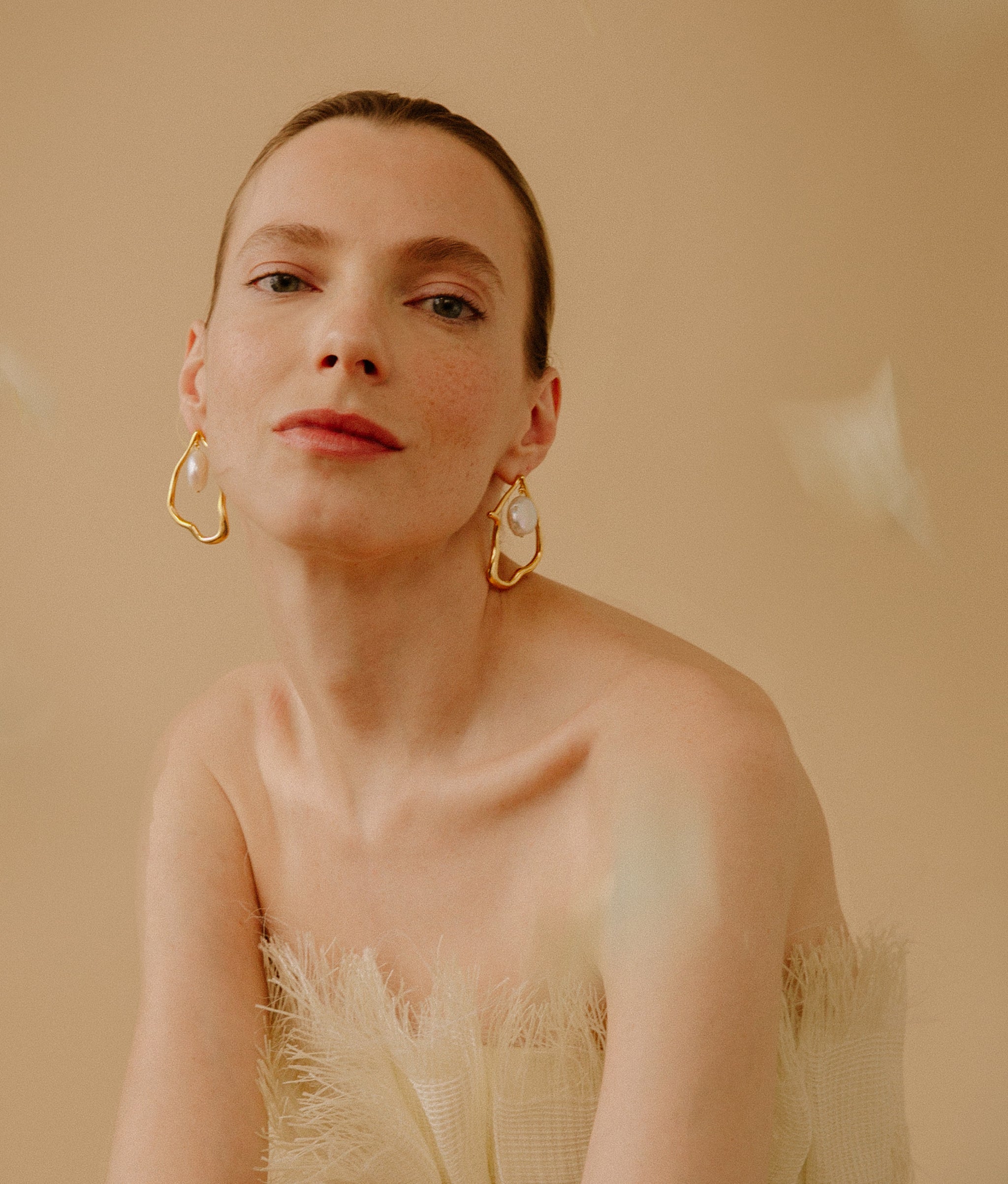 Model wearing the Formation Earrings in Pearl on a tan background.
