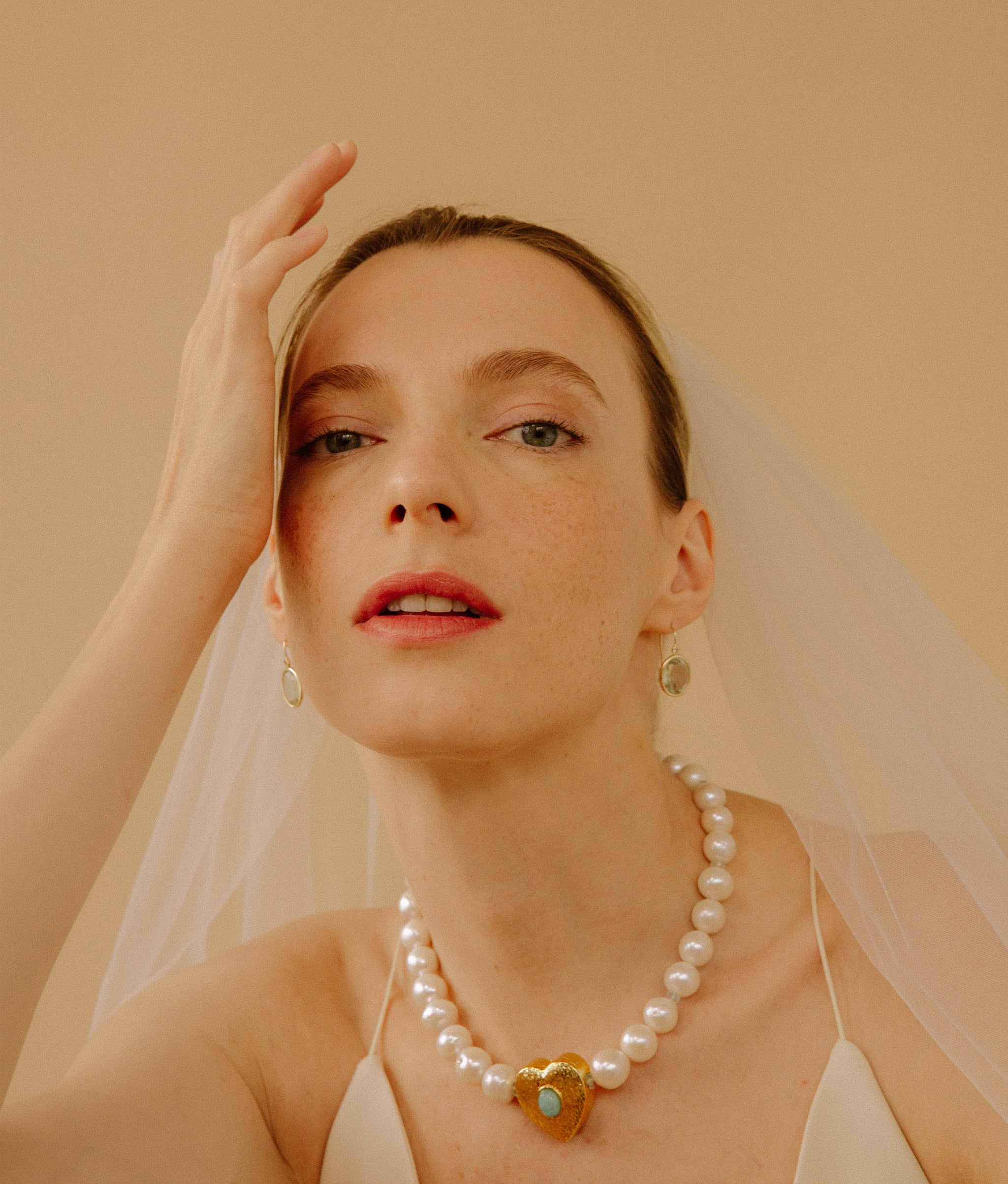 Model on a tan background wearing the Gemini Collar in Pearl and the 14k Gold Pool Earrings in Green Amethyst & Diamond.