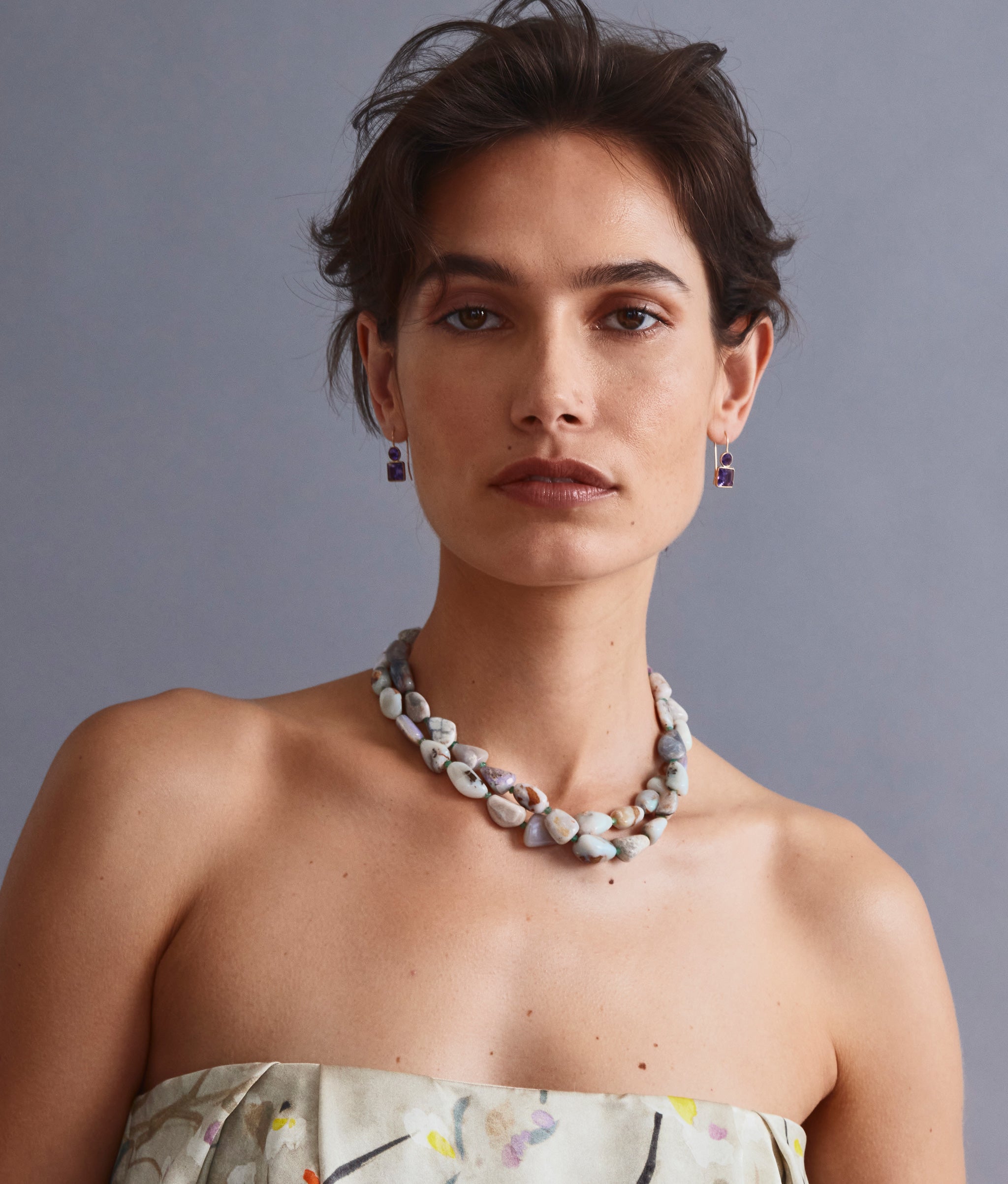 Model on grey backdrop wears Pastille Earrings in Amethyst with fine necklaces.
