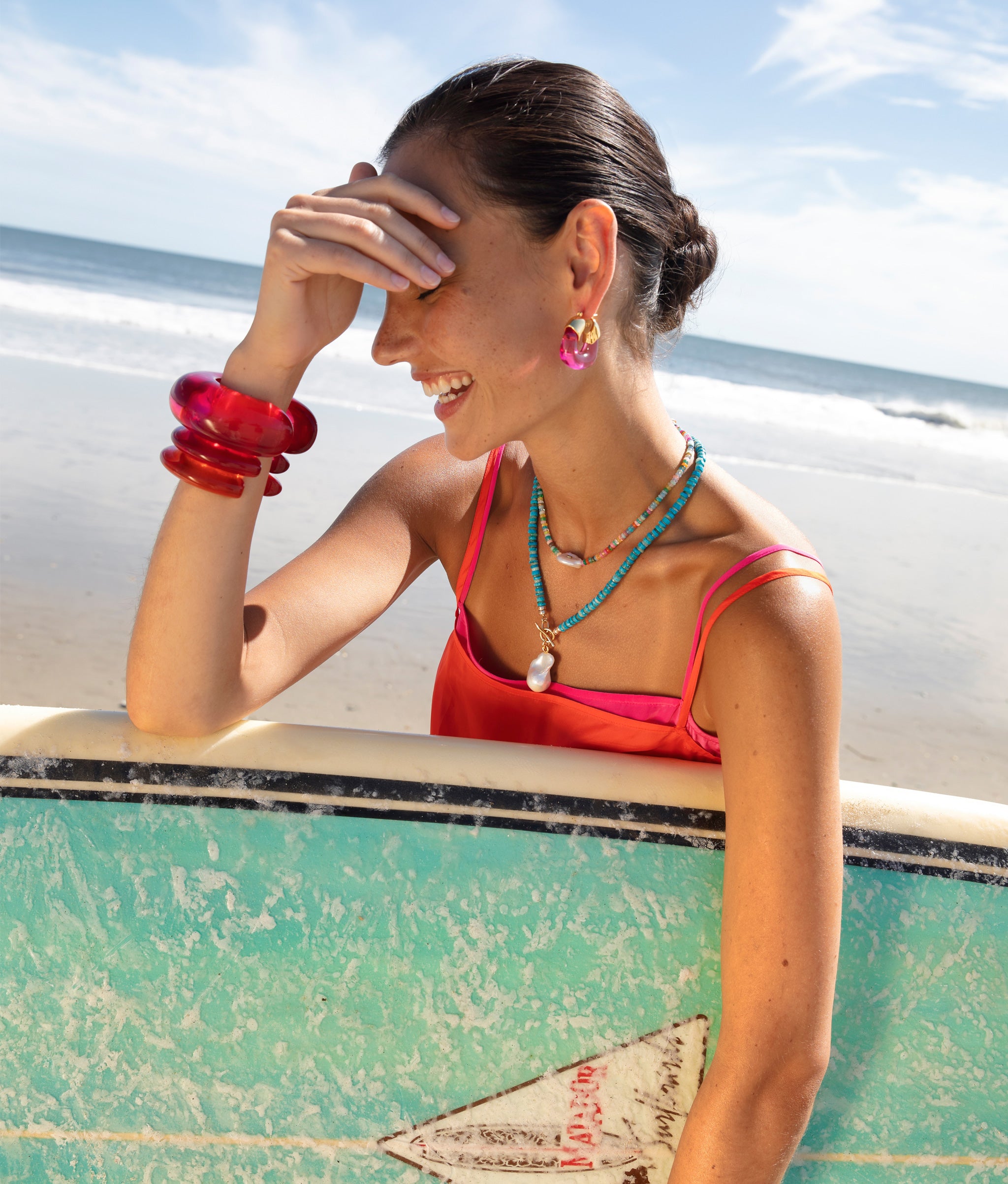 Model at the beach wearing Arc and Ridge Cuffs in Magenta and Persimmon, Organic Hoops in Flamingo, Pearl Isle Necklace.