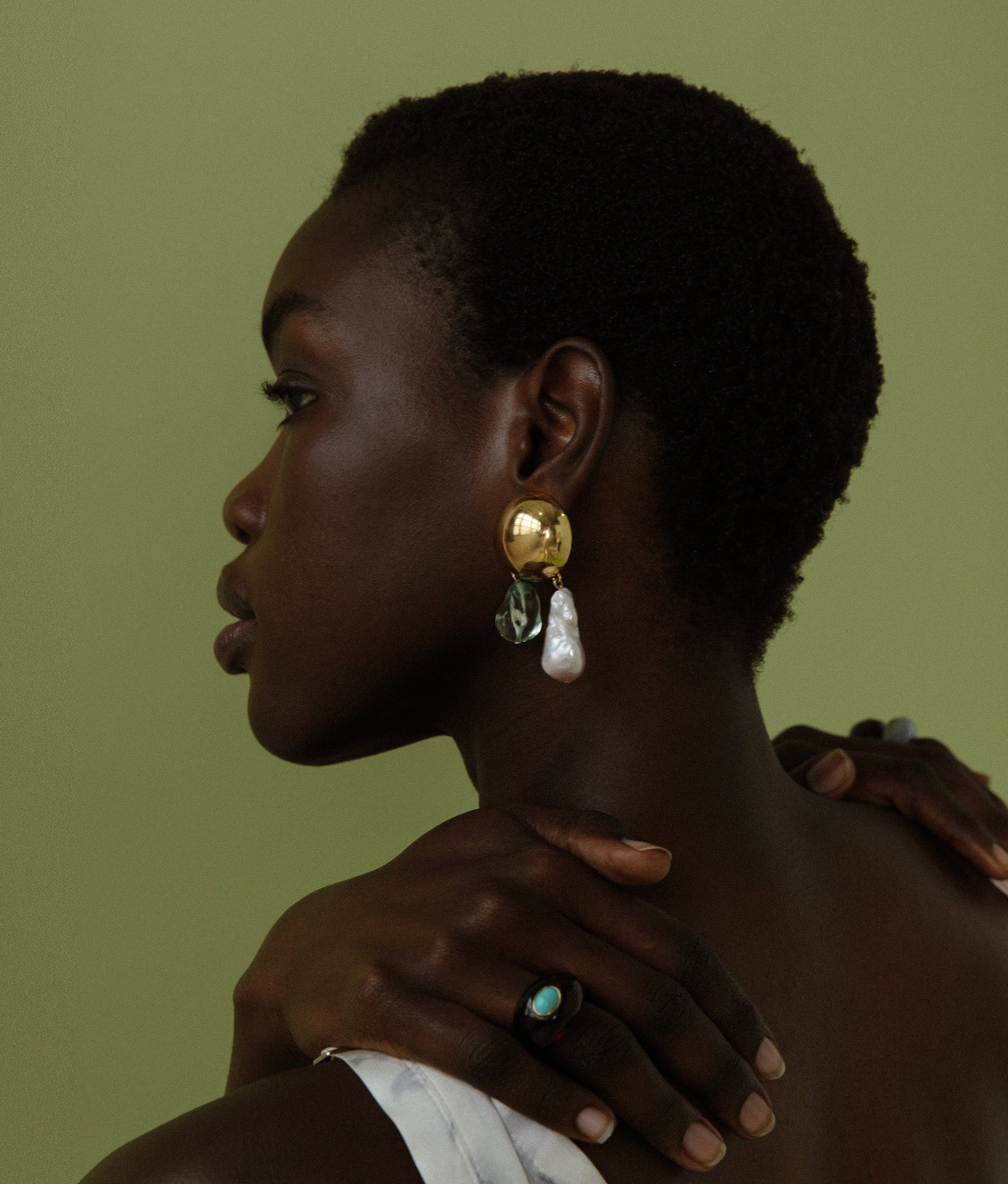 Close-up of model in profile on green backdrop, wearing Cascada Earrings and Monument Ring.