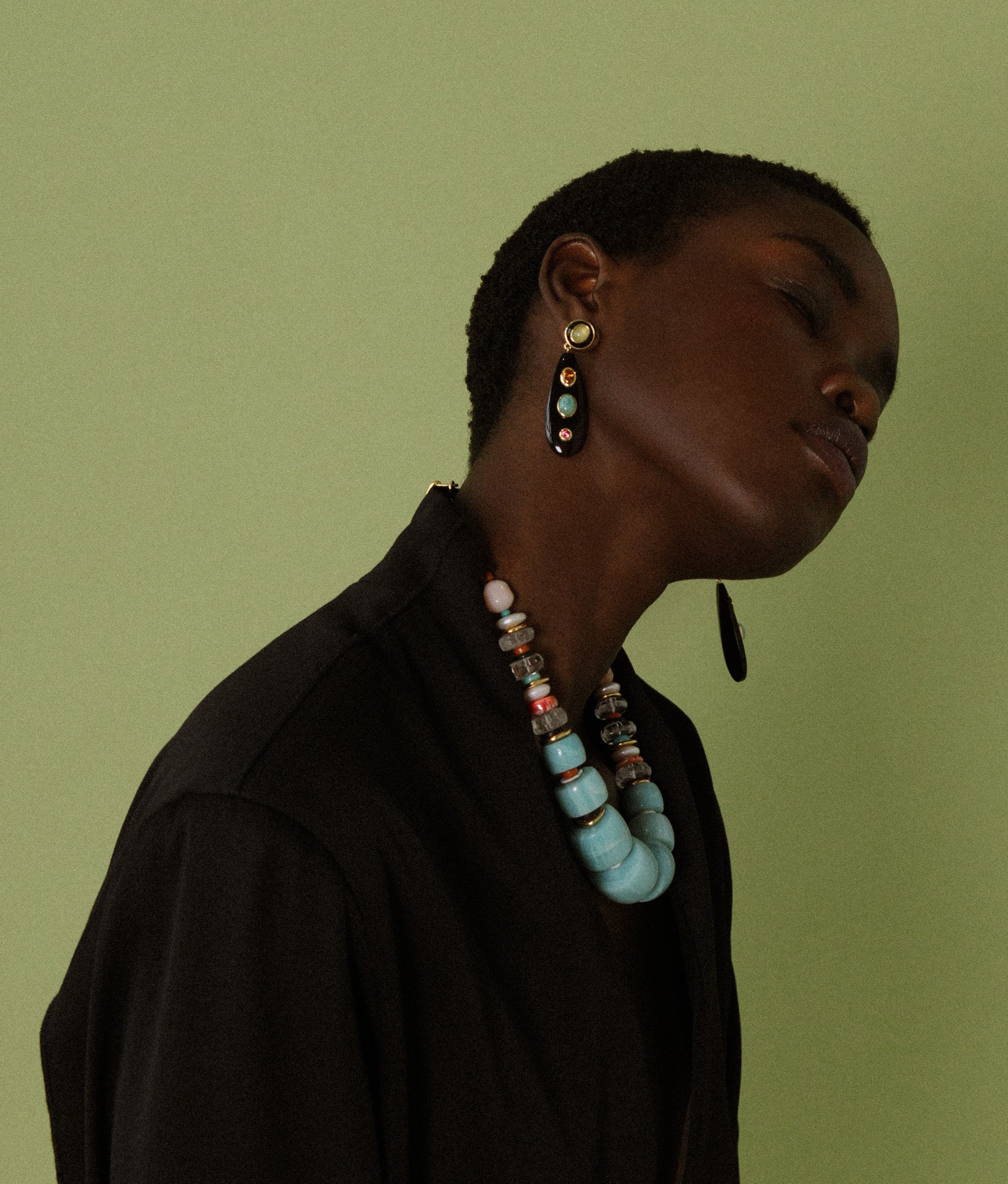 Model in profile on green backdrop wears black blazer with Regal Garden Necklace and Torre Earrings.