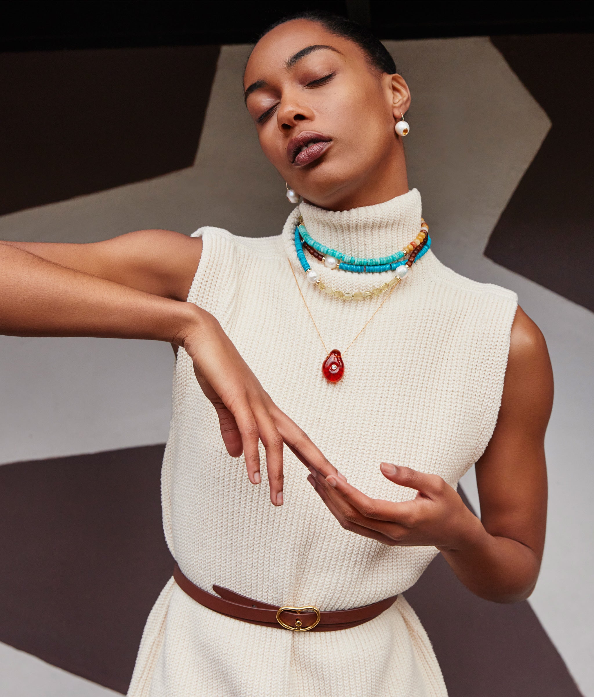 Model in cream knit dress wears Cabana Necklace in Lagoon and Muse Pendant in Amber Brown.